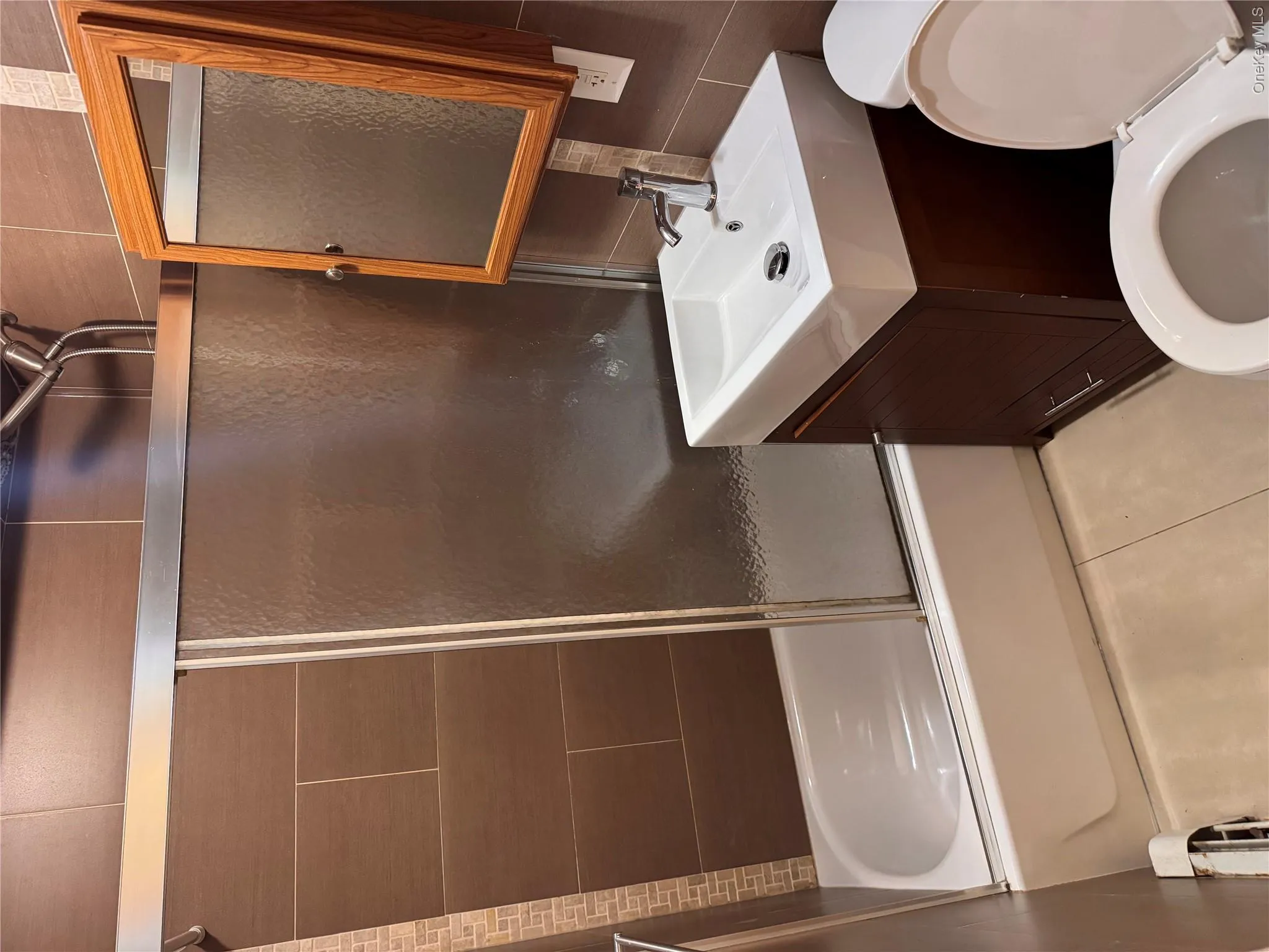 Bathtub with sliding glass enclosure, brown tile surround, and mosaic accent Bathtub with sliding glass enclosure, brown tile surround, and mosaic accent