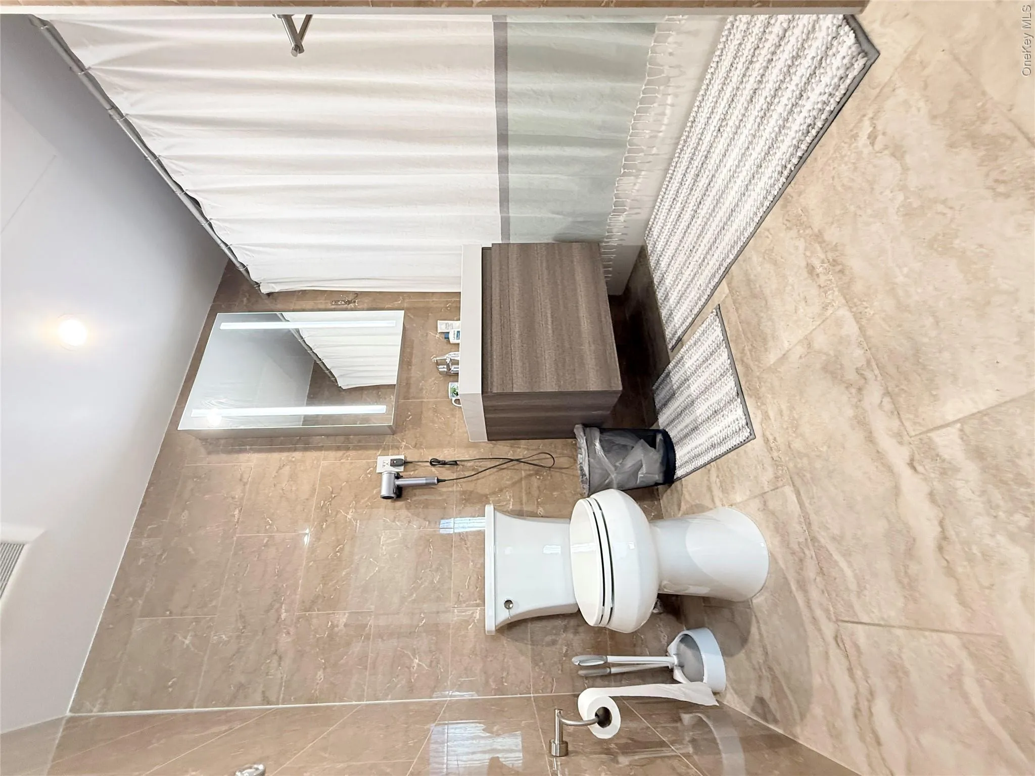 Wall-to-wall stone-finish tile, floating vanity with an integrated sink, illuminated mirror, and a built-in toilet Wall-to-wall stone-finish tile, floating vanity with an integrated sink, illuminated mirror, and a built-in toilet