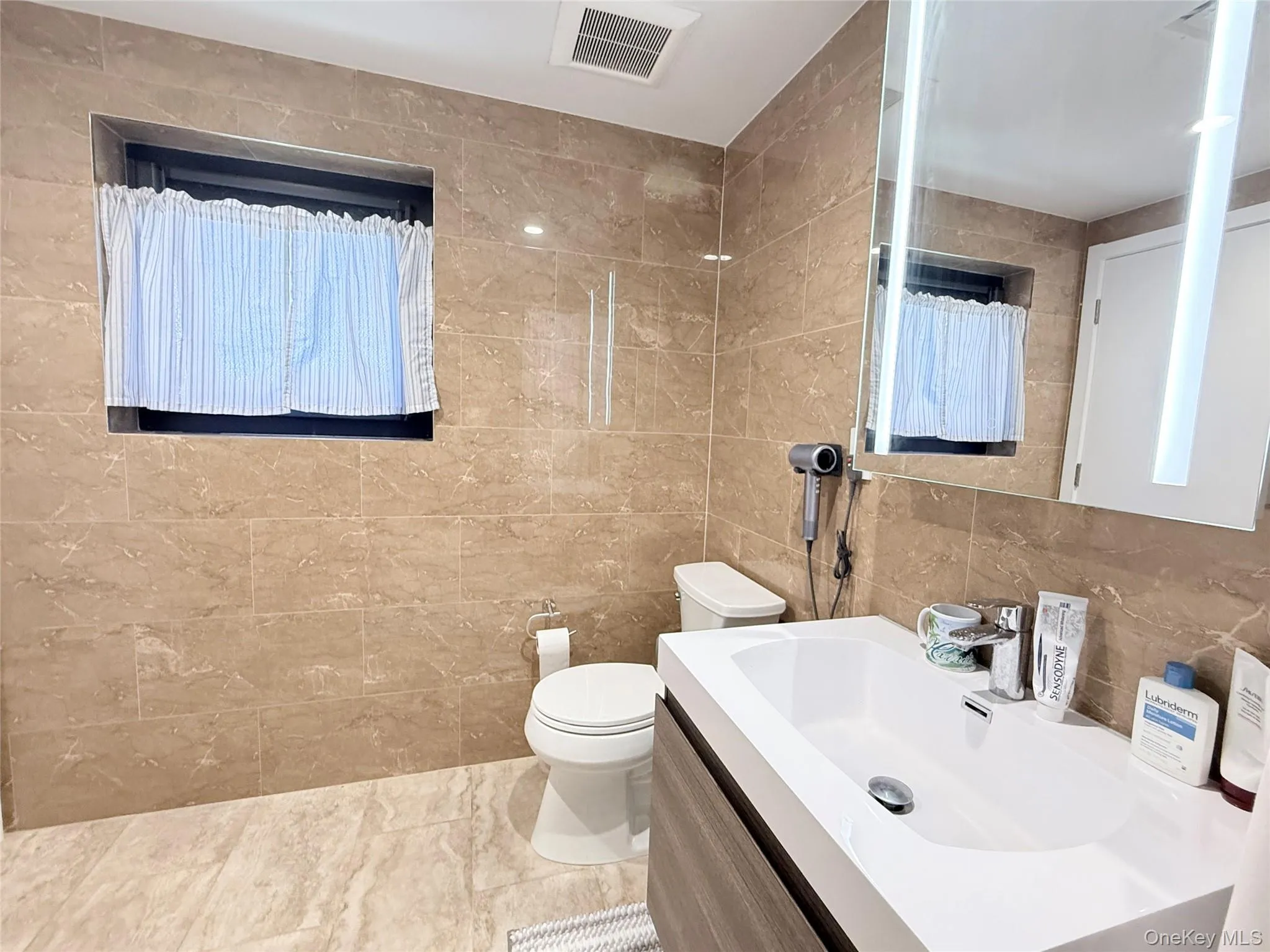 Tiled flooring and walls, modern vanity with an integrated sink, and an illuminated mirror Tiled flooring and walls, modern vanity with an integrated sink, and an illuminated mirror