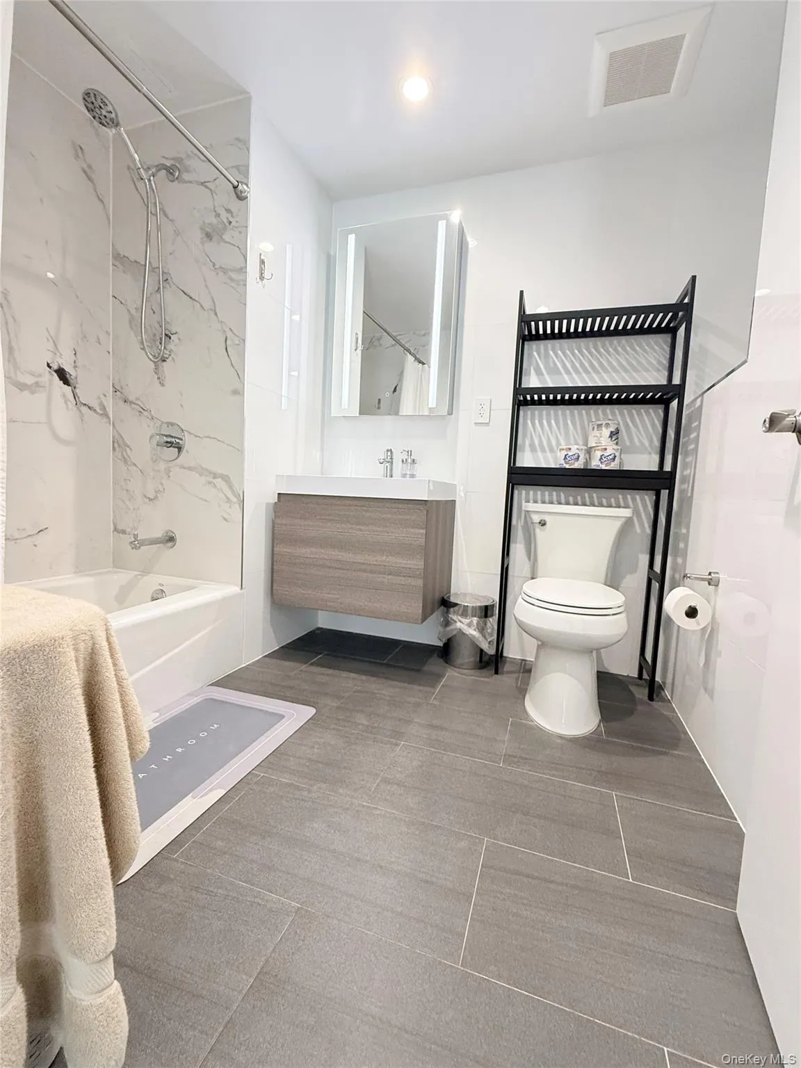 Tiled flooring leading to a bathtub with a marble-patterned tile surround Tiled flooring leading to a bathtub with a marble-patterned tile surround