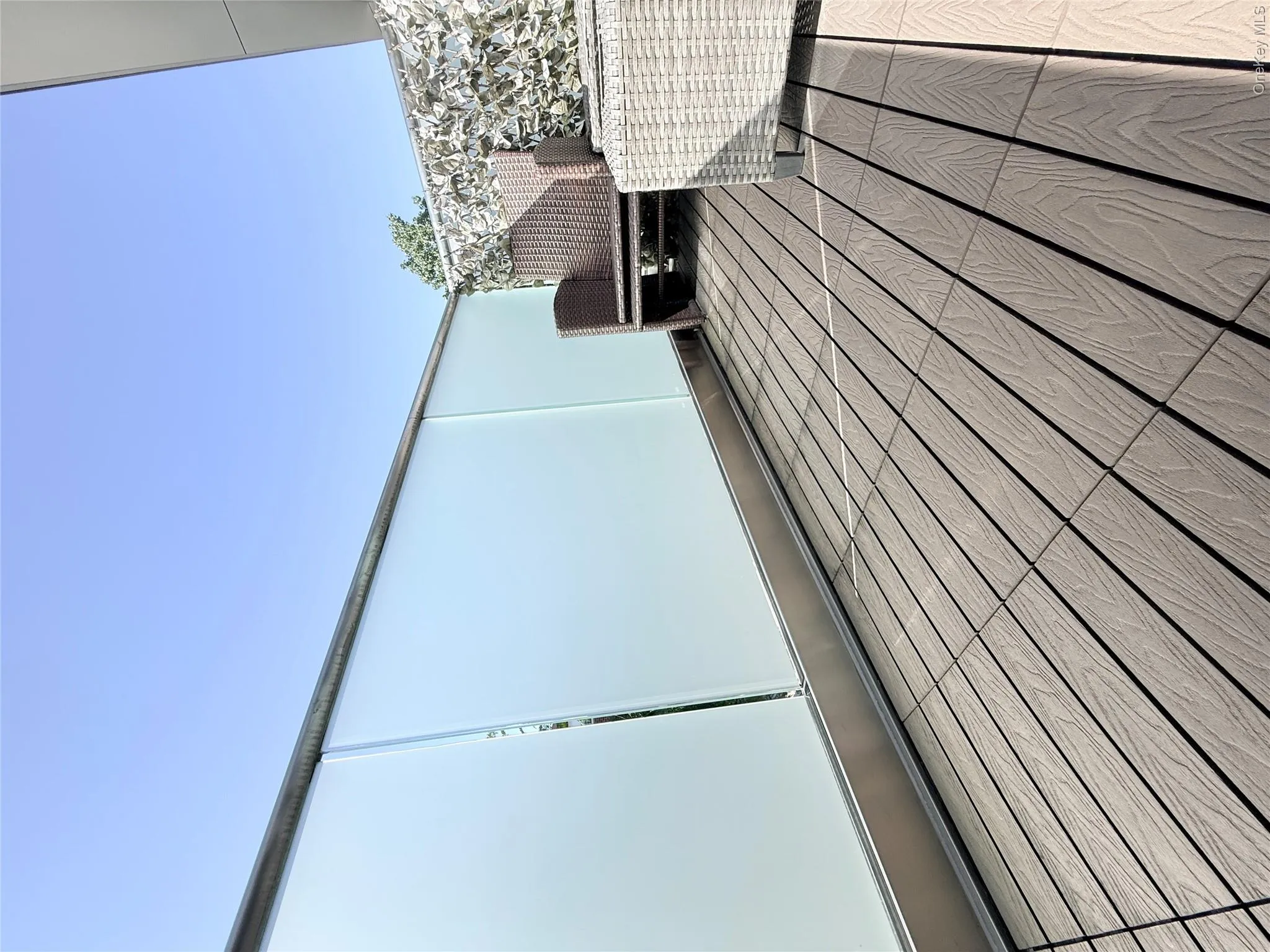 Balcony featuring wood-finish decking, a frosted glass privacy railing, and an architectural feature wall Balcony featuring wood-finish decking, a frosted glass privacy railing, and an architectural feature wall