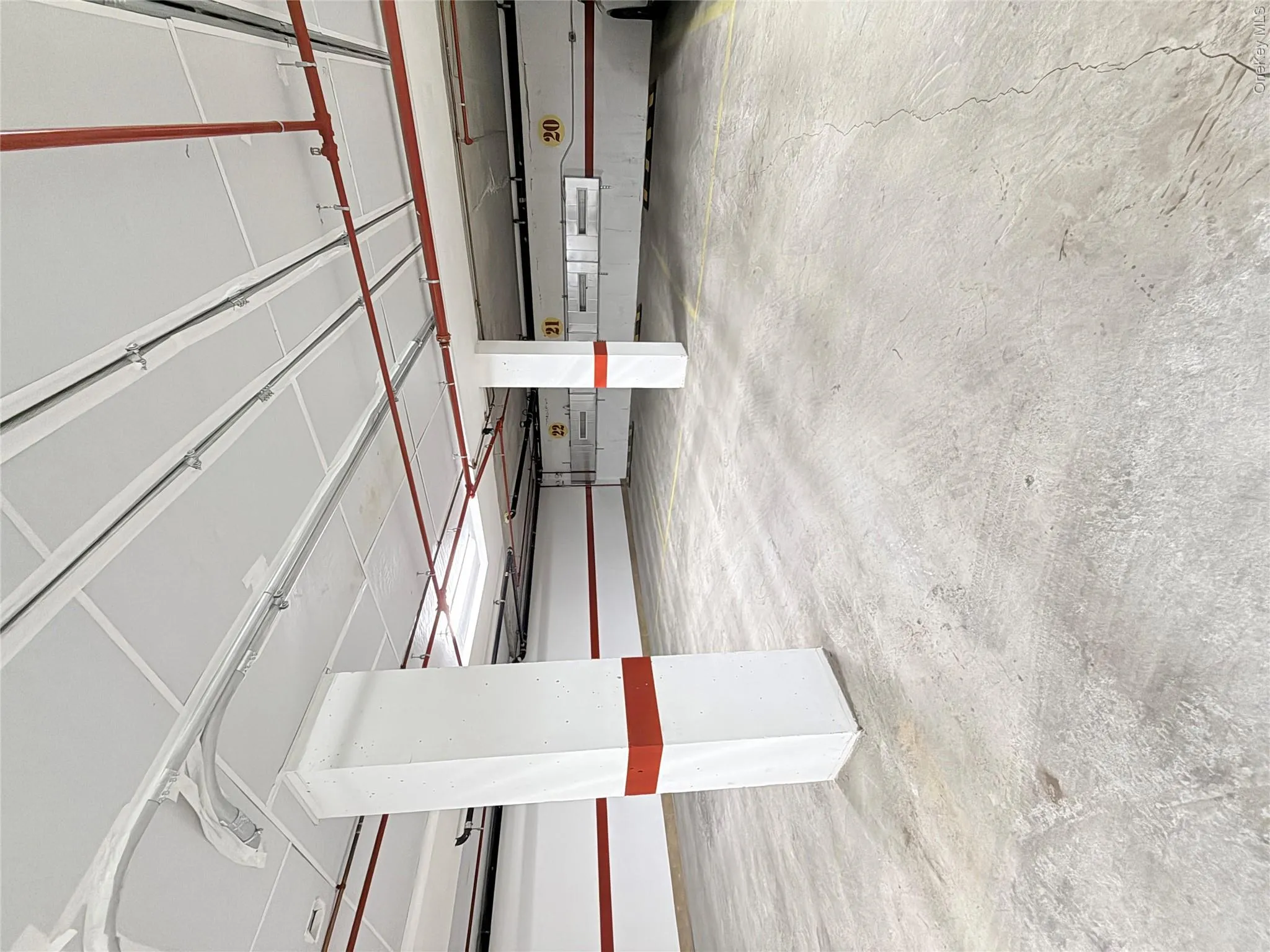 Spacious parking area featuring concrete flooring, exposed overhead piping, and painted structural columns Spacious parking area featuring concrete flooring, exposed overhead piping, and painted structural columns
