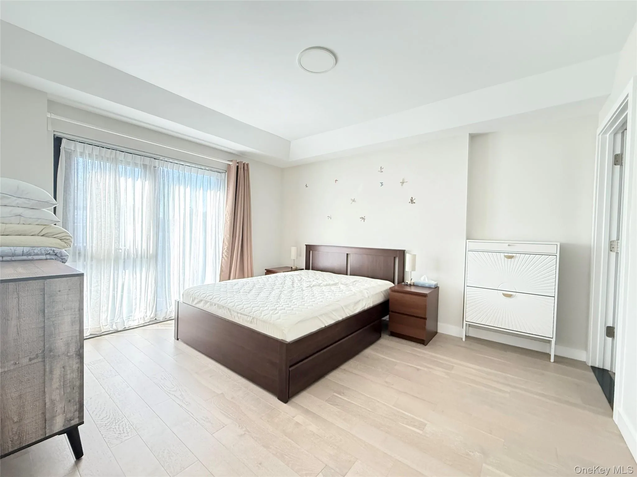 Light wood-finish flooring, recessed ceiling lighting, full-height window with sheer and blackout drapery, and white painted walls Light wood-finish flooring, recessed ceiling lighting, full-height window with sheer and blackout drapery, and white painted walls