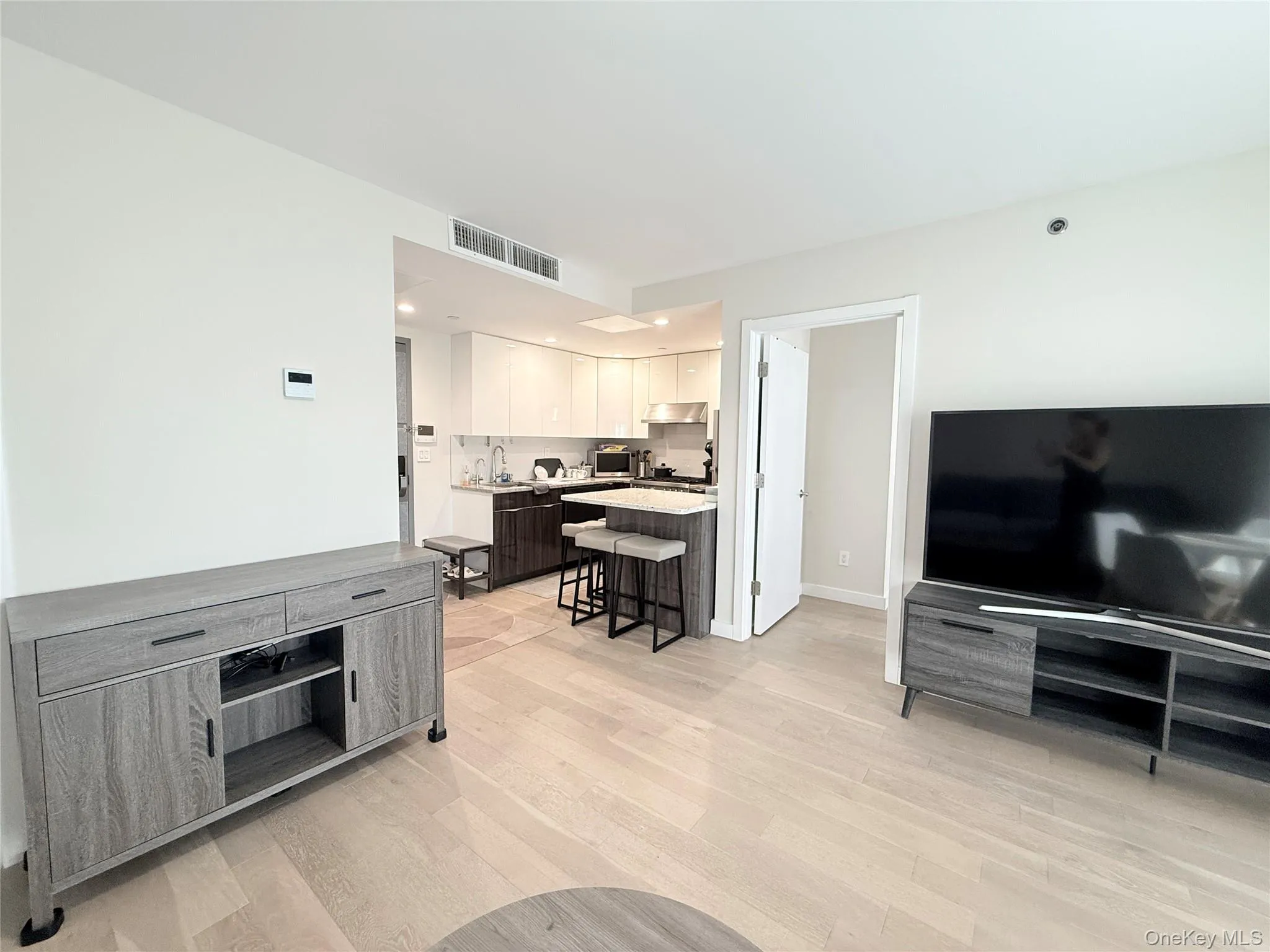 Light wood-finish flooring throughout, integrated kitchen with a breakfast bar, white upper cabinetry, and dark lower cabinetry Light wood-finish flooring throughout, integrated kitchen with a breakfast bar, white upper cabinetry, and dark lower cabinetry
