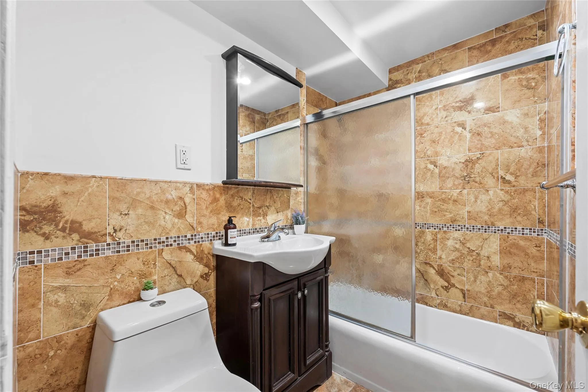 Bathroom featuring full-height tiled walls, a vanity with integrated sink, a built-in bathtub, and a framed mirror Bathroom featuring full-height tiled walls, a vanity with integrated sink, a built-in bathtub, and a framed mirror