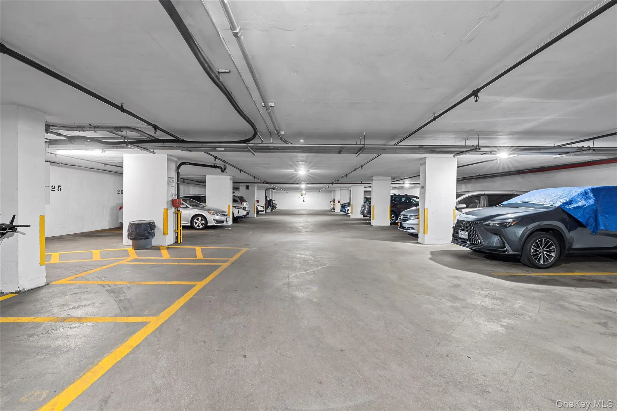 Underground parking area featuring concrete flooring, structural columns, and overhead lighting Underground parking area featuring concrete flooring, structural columns, and overhead lighting