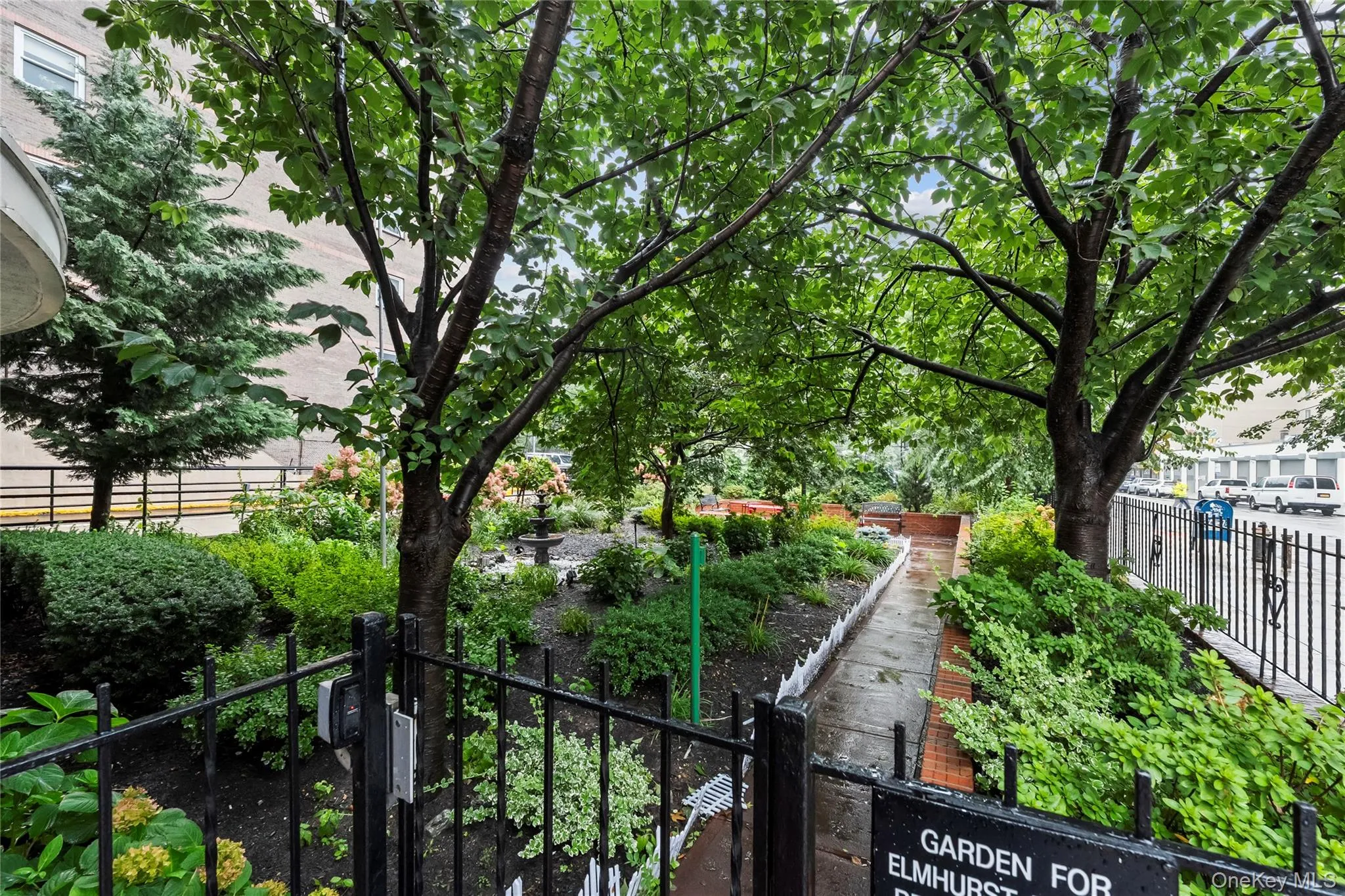 Garden area featuring mature trees, diverse plantings, and a paved pathway Garden area featuring mature trees, diverse plantings, and a paved pathway