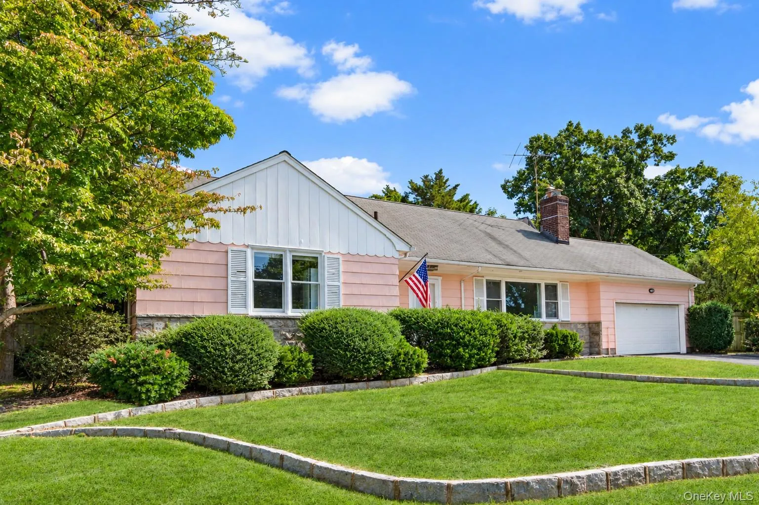 Single-story exterior with a pitched roof, stone foundation, attached garage with a roll-up door, and mature landscaping Single-story exterior with a pitched roof, stone foundation, attached garage with a roll-up door, and mature landscaping