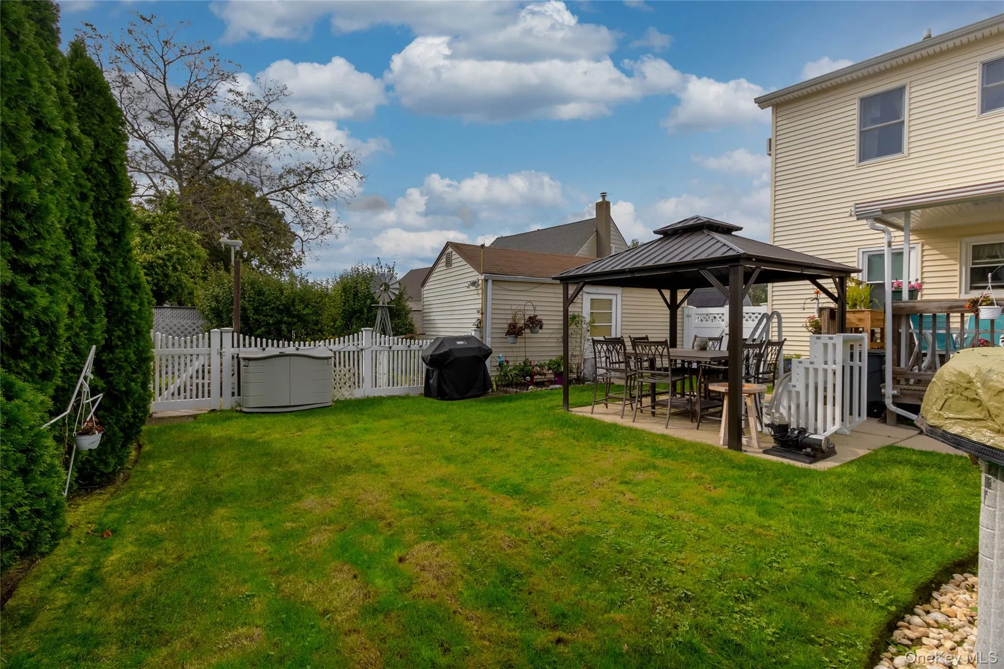 Expansive green lawn with a privacy hedge, white picket fencing, and a paved patio area Expansive green lawn with a privacy hedge, white picket fencing, and a paved patio area