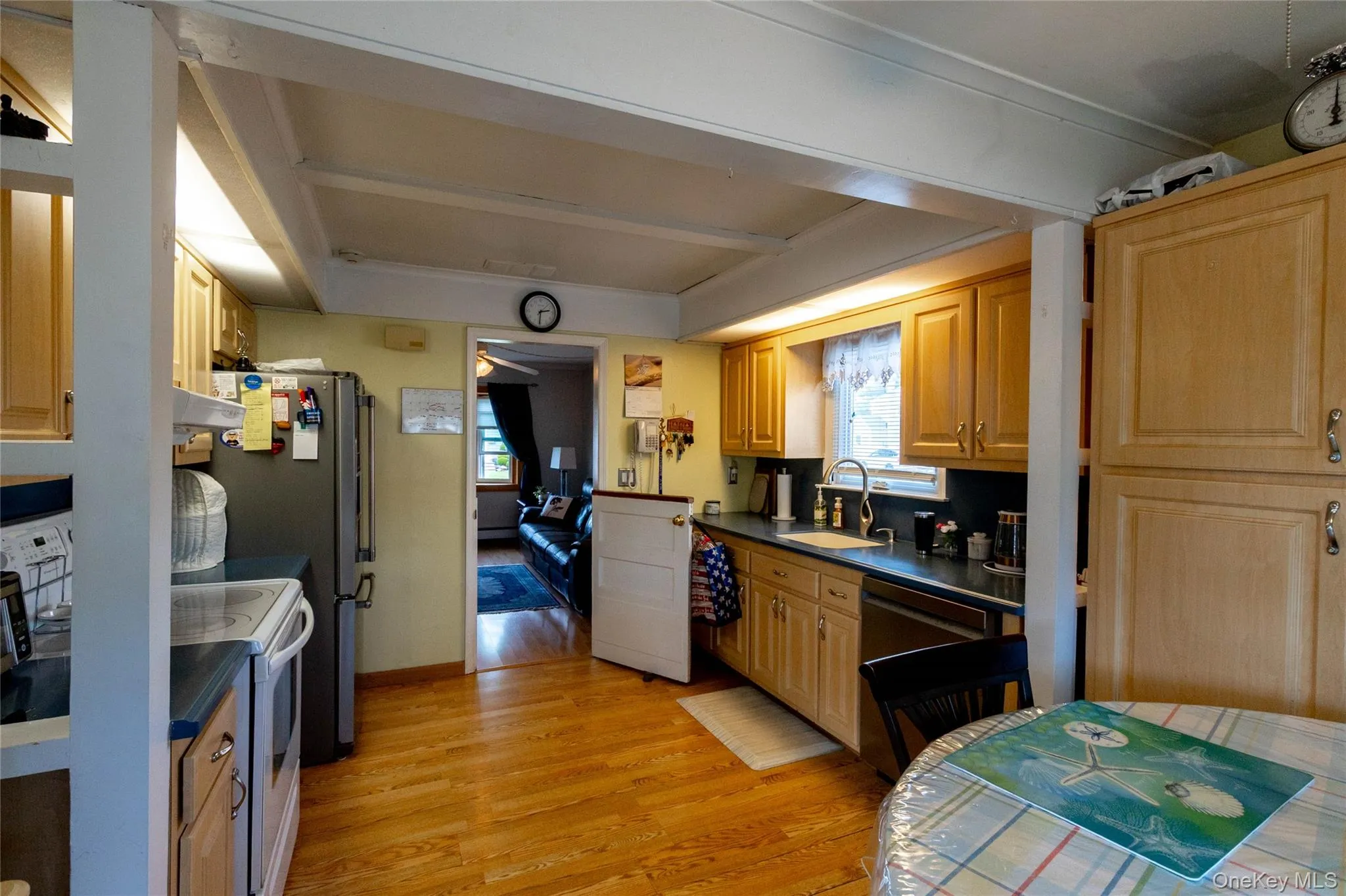 Wood-finish flooring, exposed ceiling beams, light wood-finish cabinetry, black countertops, and a stainless steel sink Wood-finish flooring, exposed ceiling beams, light wood-finish cabinetry, black countertops, and a stainless steel sink
