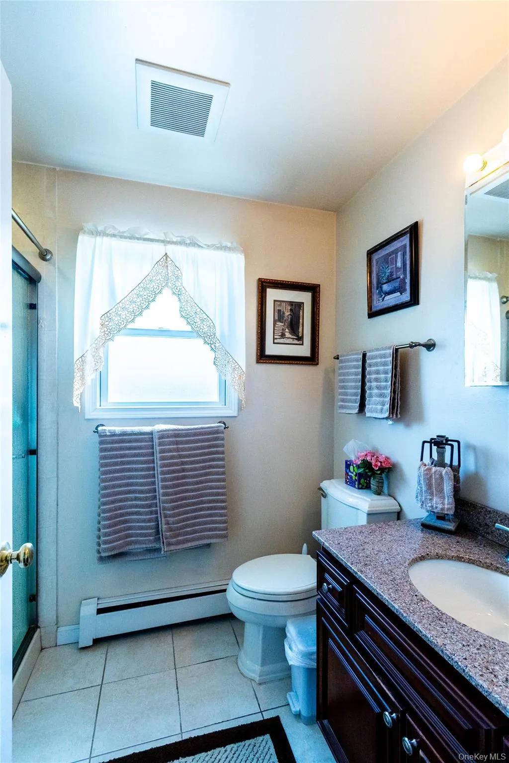 Bathroom featuring a dark wood-finish vanity with an integrated sink and granite-finish countertop, tiled flooring, and a window with natural light Bathroom featuring a dark wood-finish vanity with an integrated sink and granite-finish countertop, tiled flooring, and a window with natural light