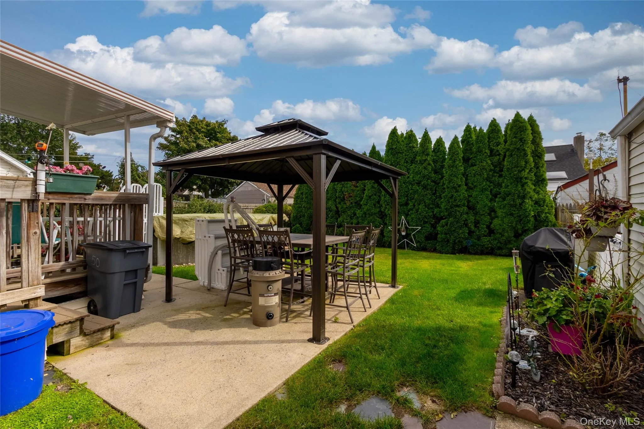 Expansive backyard featuring a concrete patio, freestanding gazebo, manicured lawn, and mature privacy trees Expansive backyard featuring a concrete patio, freestanding gazebo, manicured lawn, and mature privacy trees