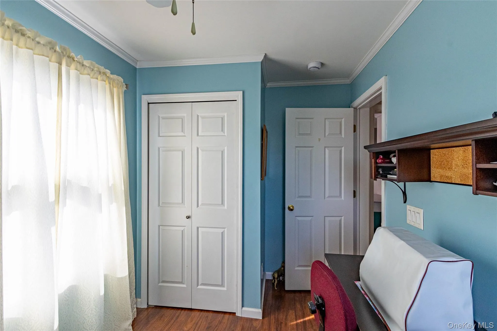Wood-finish flooring, white bi-fold closet doors, white paneled interior door, crown molding, and built-in shelving unit Wood-finish flooring, white bi-fold closet doors, white paneled interior door, crown molding, and built-in shelving unit