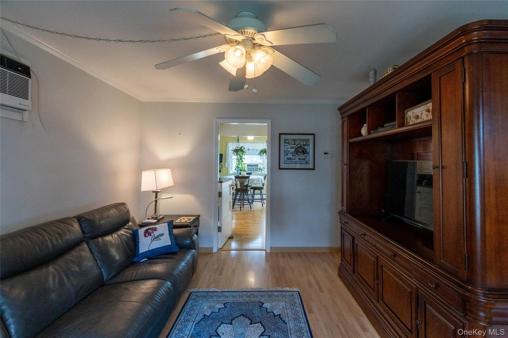 Wood-finish flooring throughout, ceiling fan with integrated lighting, and a built-in wood entertainment center with display shelving Wood-finish flooring throughout, ceiling fan with integrated lighting, and a built-in wood entertainment center with display shelving