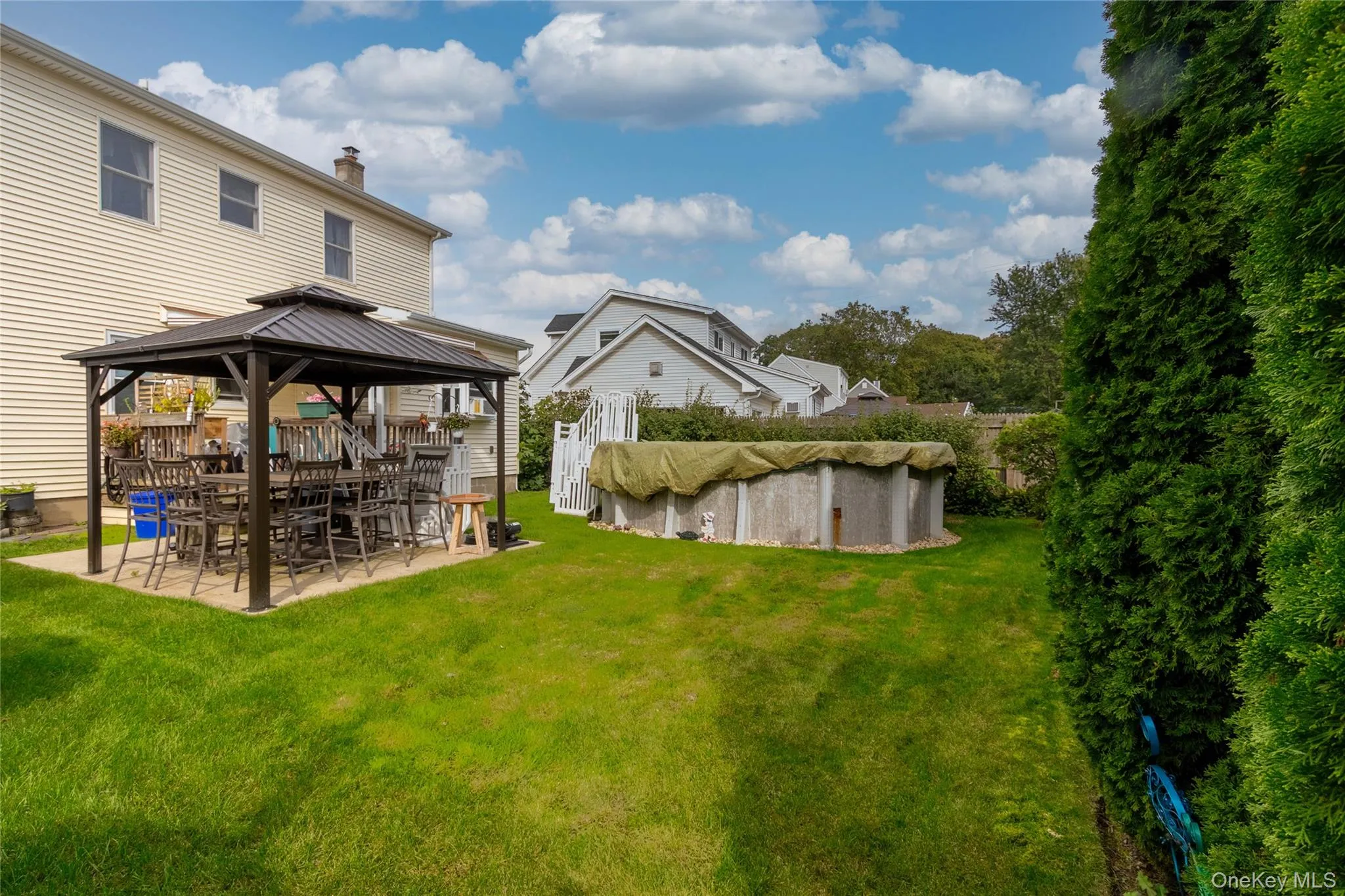 Expansive green lawn featuring a covered patio with a dark metal gazebo and an above-ground pool Expansive green lawn featuring a covered patio with a dark metal gazebo and an above-ground pool
