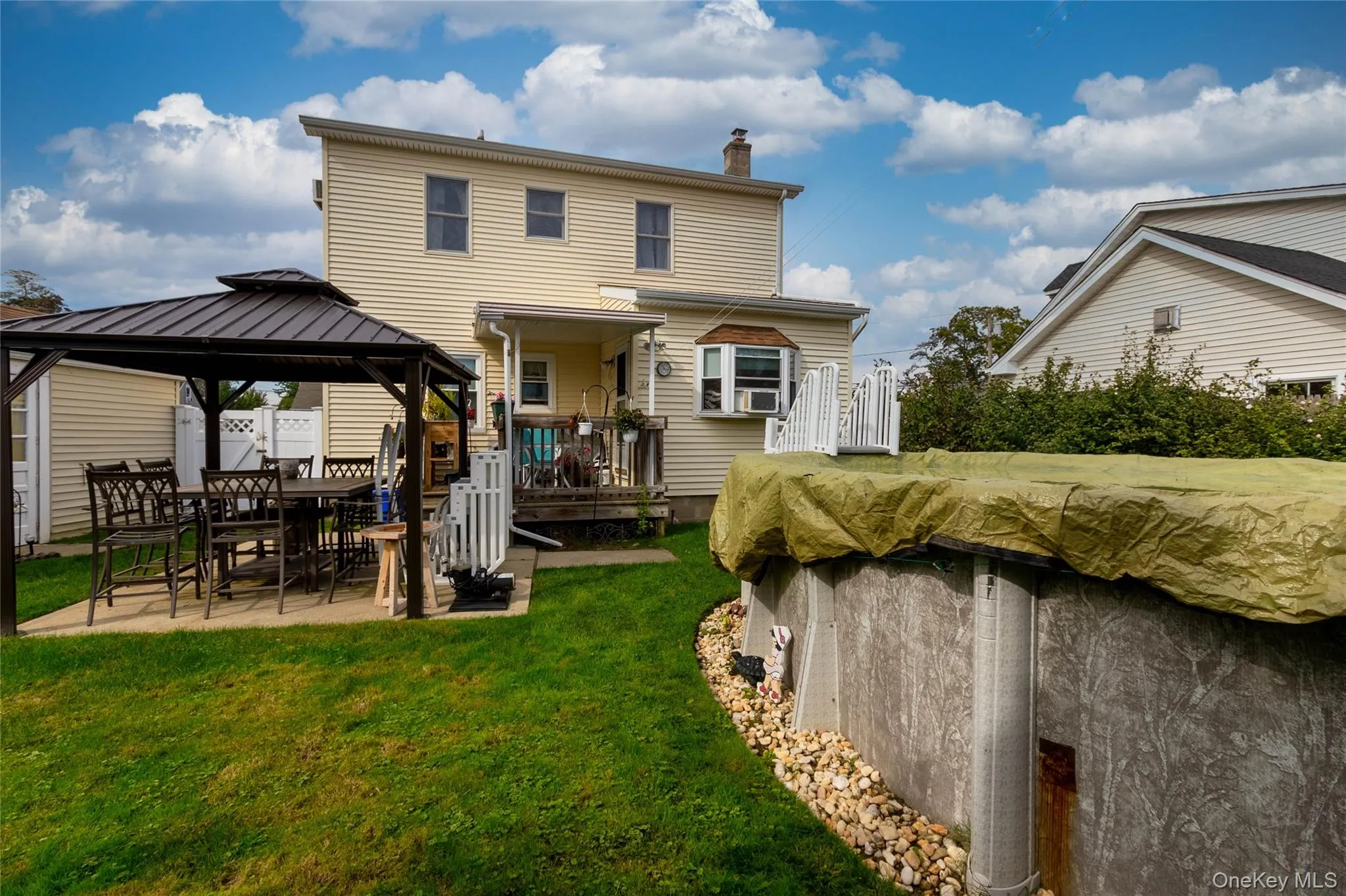 Expansive backyard featuring a covered patio, an above-ground pool, and a two-story residence with a bay window Expansive backyard featuring a covered patio, an above-ground pool, and a two-story residence with a bay window