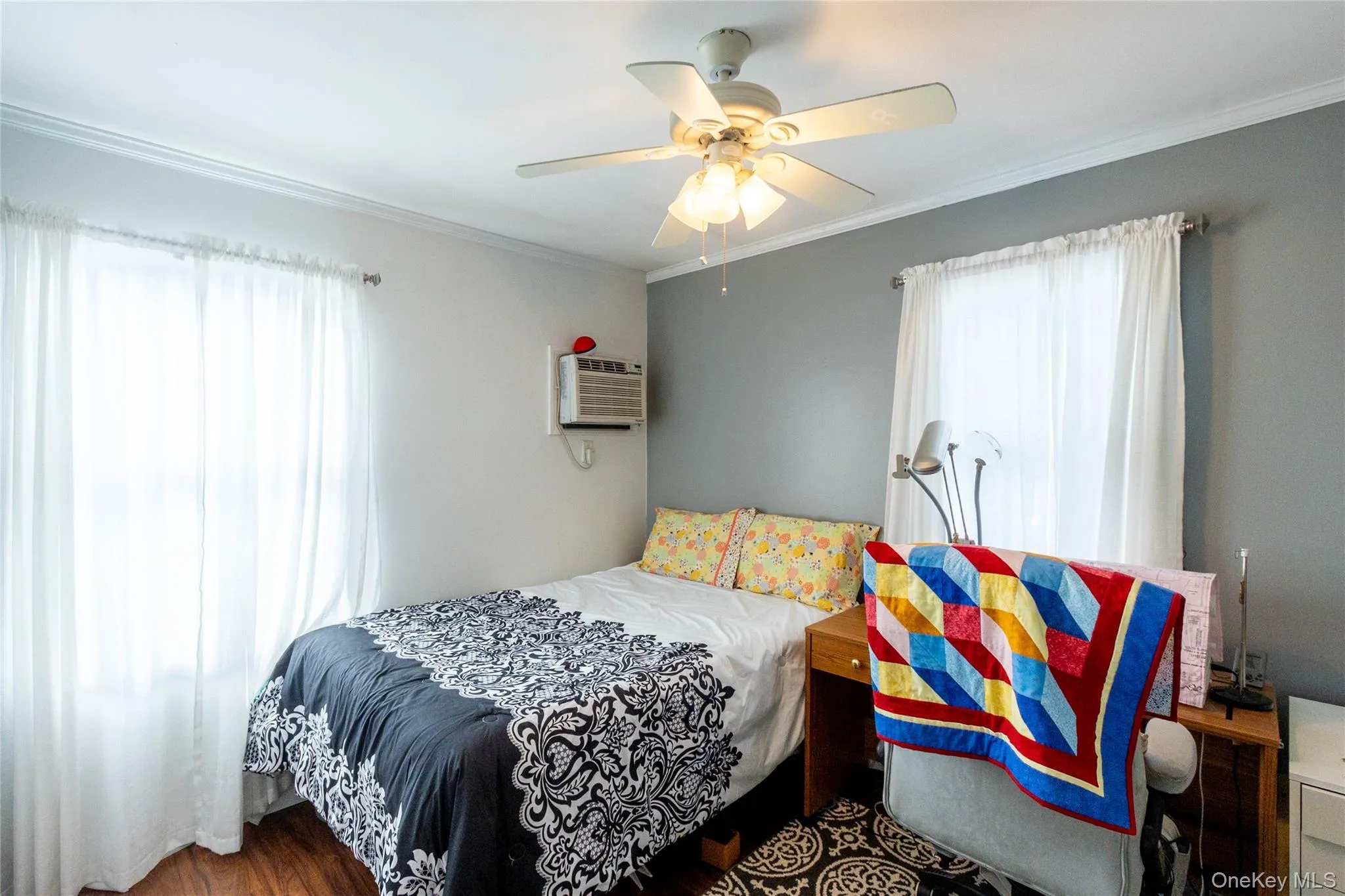 Wood-finish flooring, two windows, crown molding, and a ceiling fan with light fixture Wood-finish flooring, two windows, crown molding, and a ceiling fan with light fixture