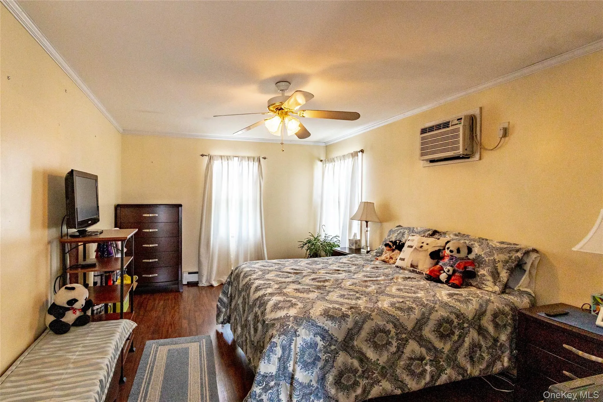 Wood-finish flooring with crown molding, ceiling fan, two windows with blinds, and wall-mounted air conditioning unit Wood-finish flooring with crown molding, ceiling fan, two windows with blinds, and wall-mounted air conditioning unit