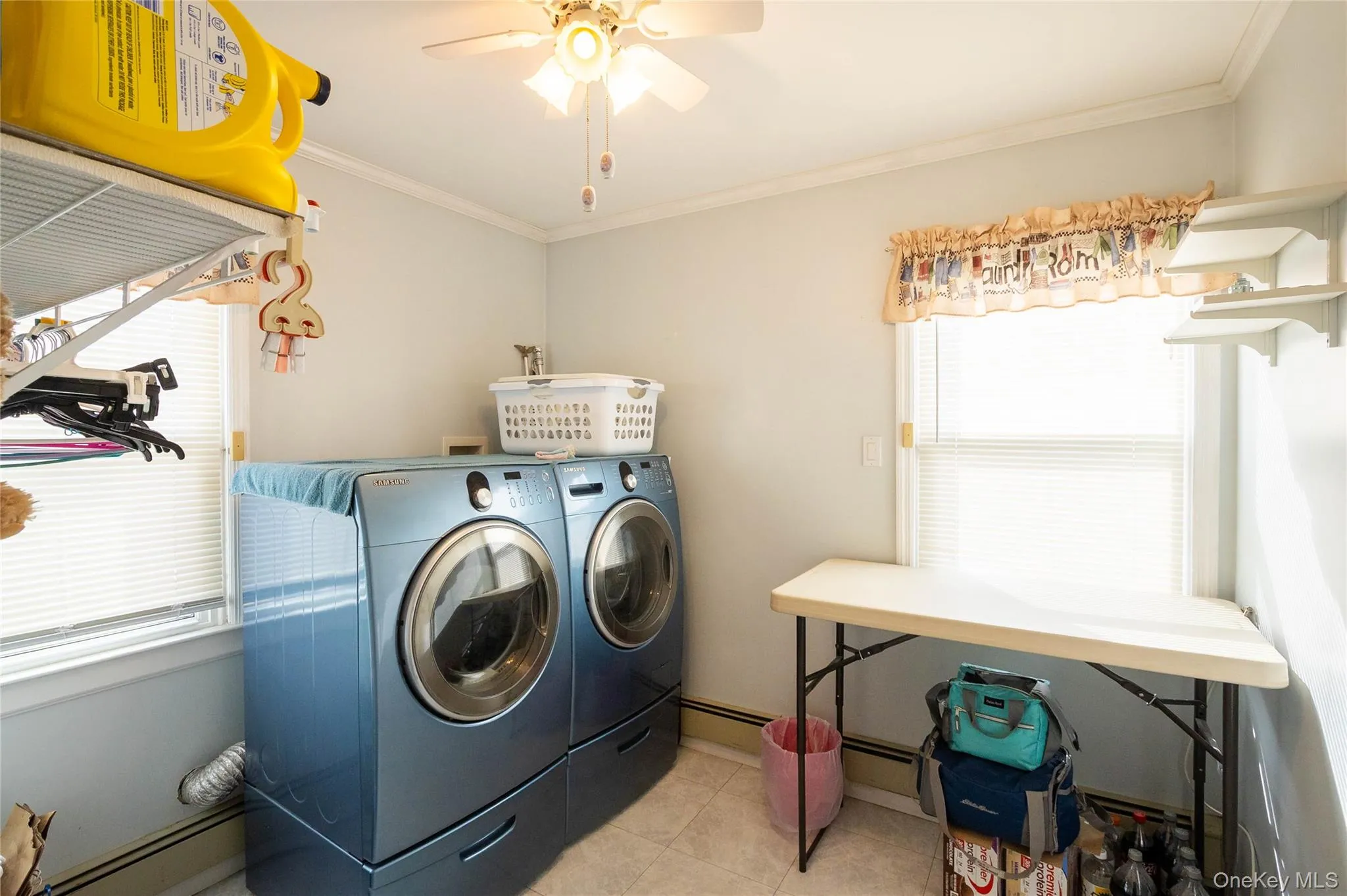 Laundry area featuring a ceiling fan, window with blinds, wall-mounted shelving, and tile flooring Laundry area featuring a ceiling fan, window with blinds, wall-mounted shelving, and tile flooring