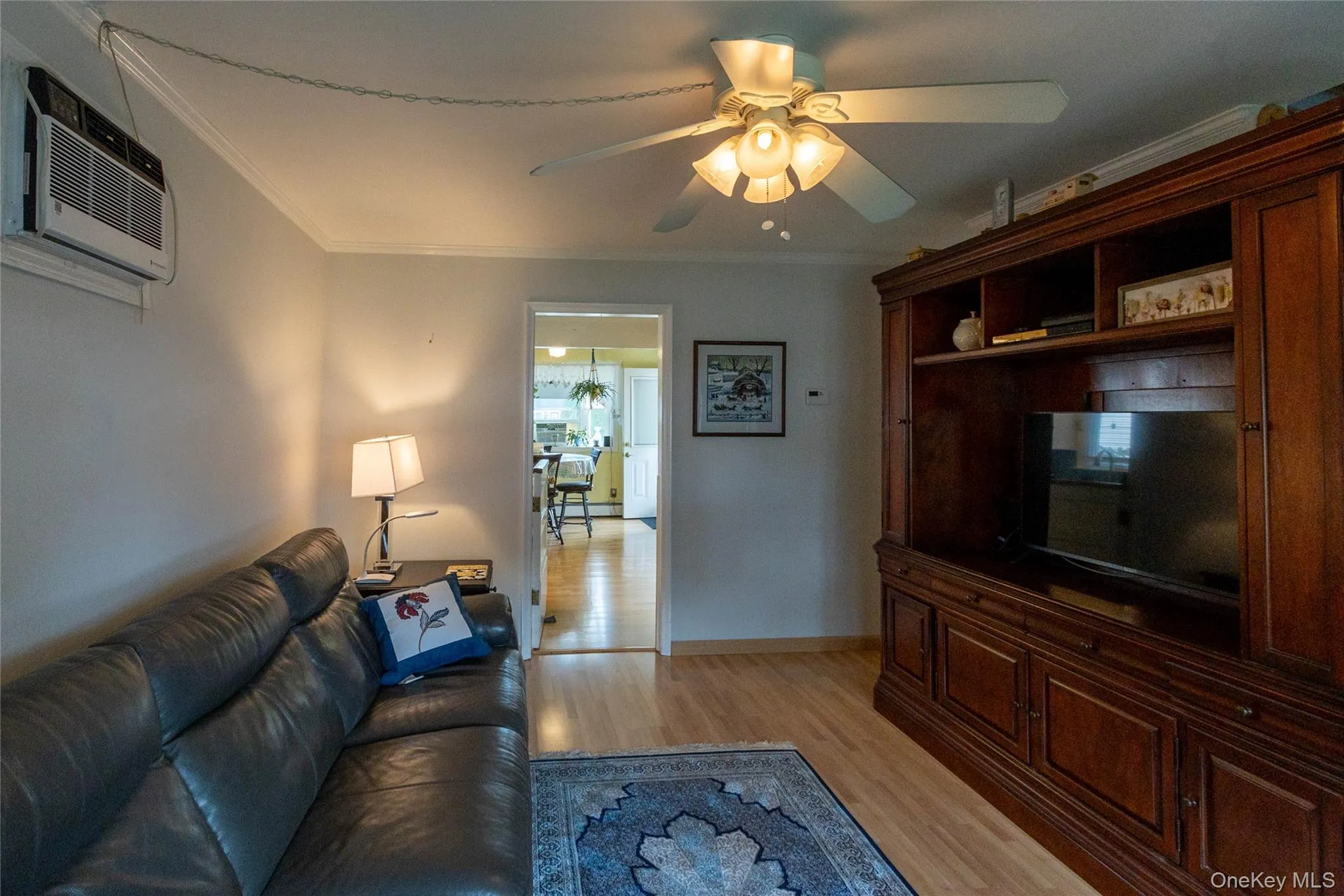 Hardwood-style flooring with a dark wood built-in media cabinet, crown molding, and a ceiling fan with integrated lighting Hardwood-style flooring with a dark wood built-in media cabinet, crown molding, and a ceiling fan with integrated lighting