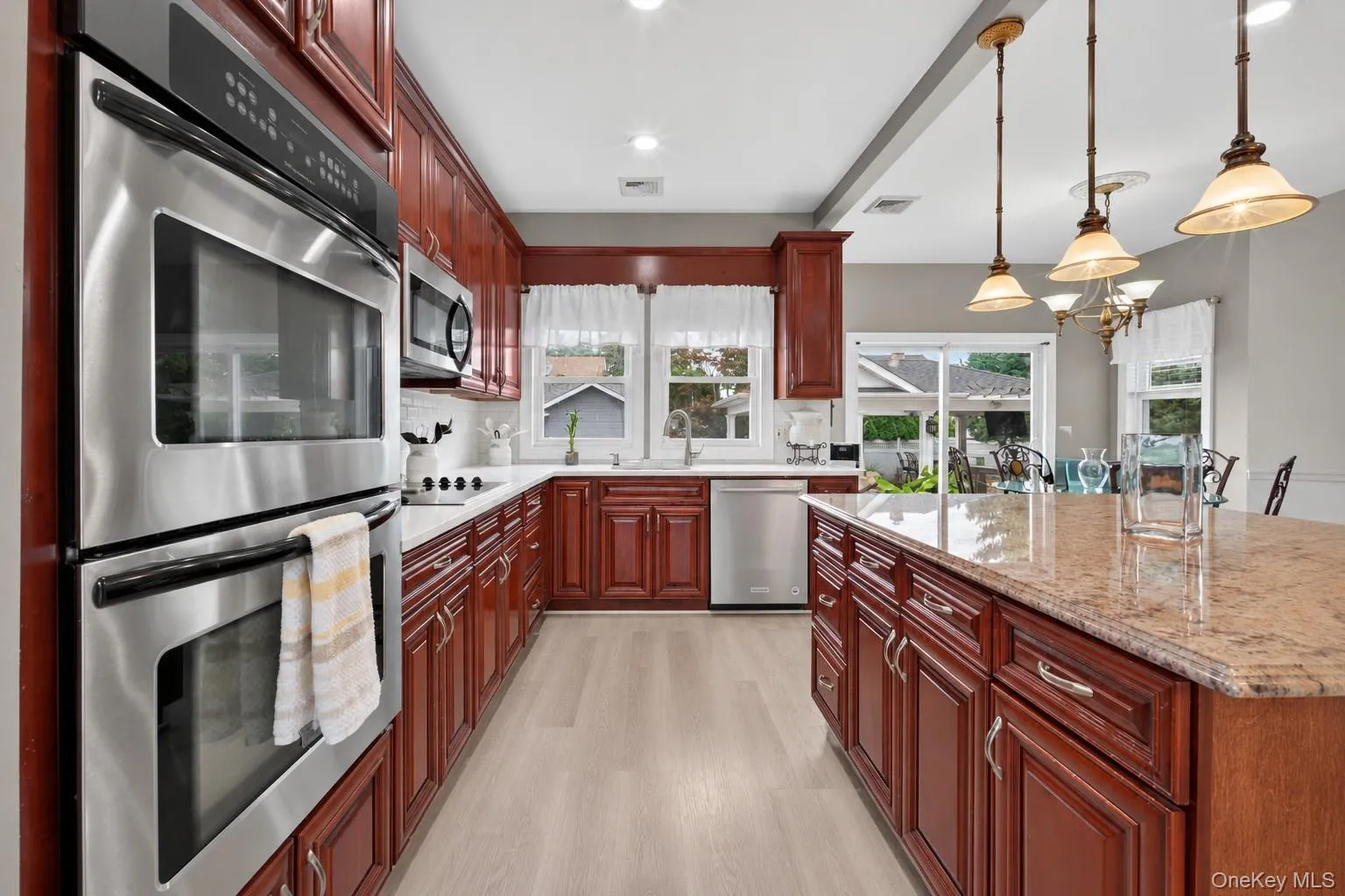 Kitchen featuring wood cabinetry, stainless steel appliances, light-toned flooring, and an island with a polished countertop Kitchen featuring wood cabinetry, stainless steel appliances, light-toned flooring, and an island with a polished countertop