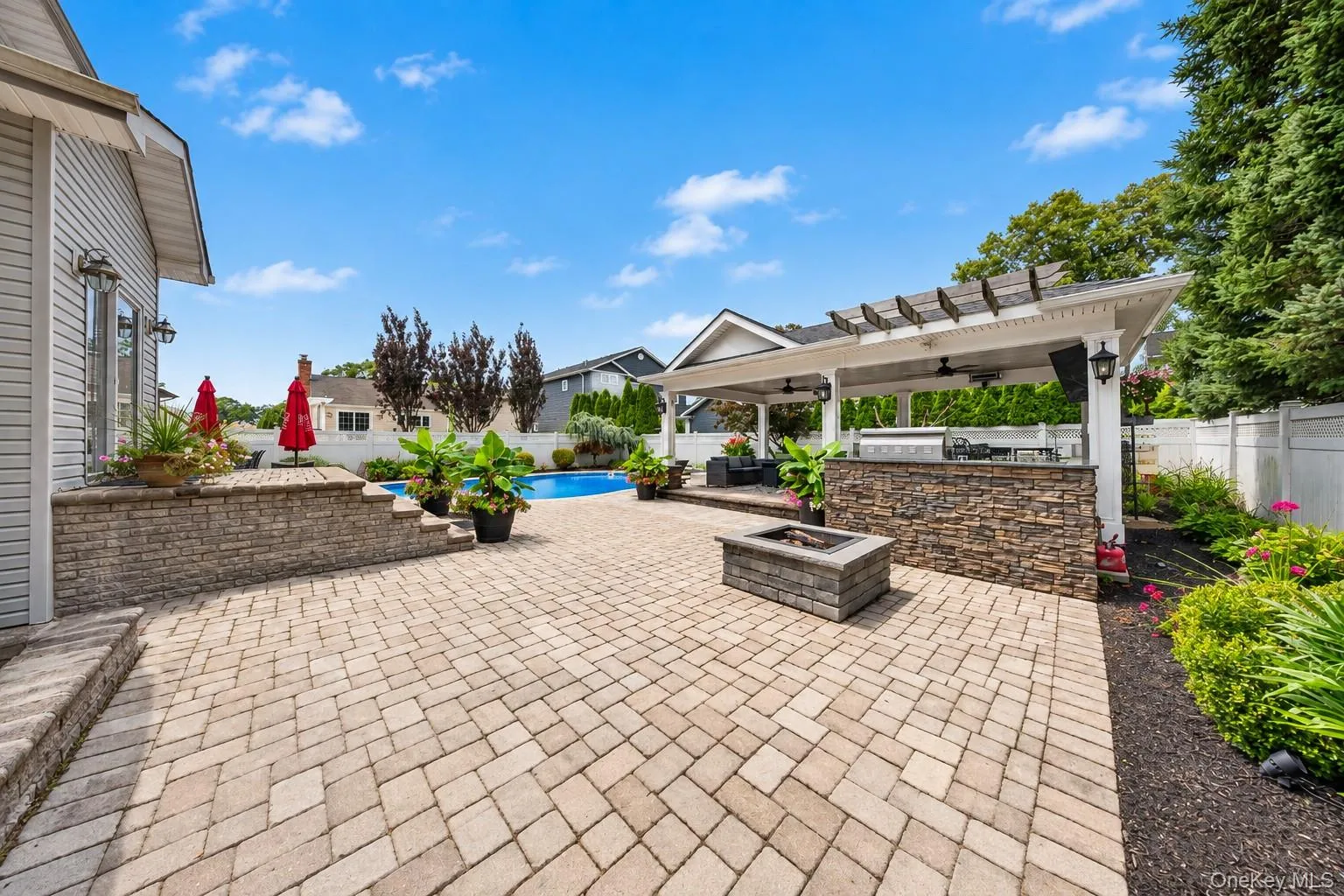 Paver patio with a stone fire pit, built-in outdoor kitchen with stone detailing, covered pergola structure, and an in-ground swimming pool Paver patio with a stone fire pit, built-in outdoor kitchen with stone detailing, covered pergola structure, and an in-ground swimming pool