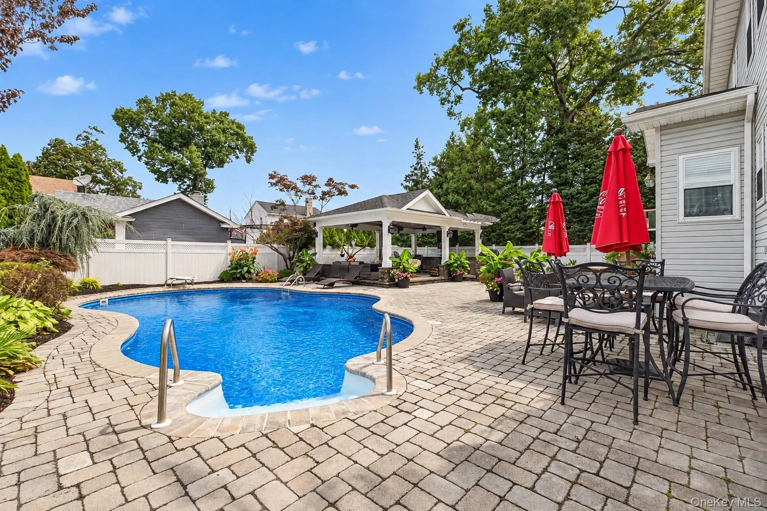 Freeform swimming pool with integrated steps, surrounded by paver patio, white privacy fence, and a covered gazebo Freeform swimming pool with integrated steps, surrounded by paver patio, white privacy fence, and a covered gazebo