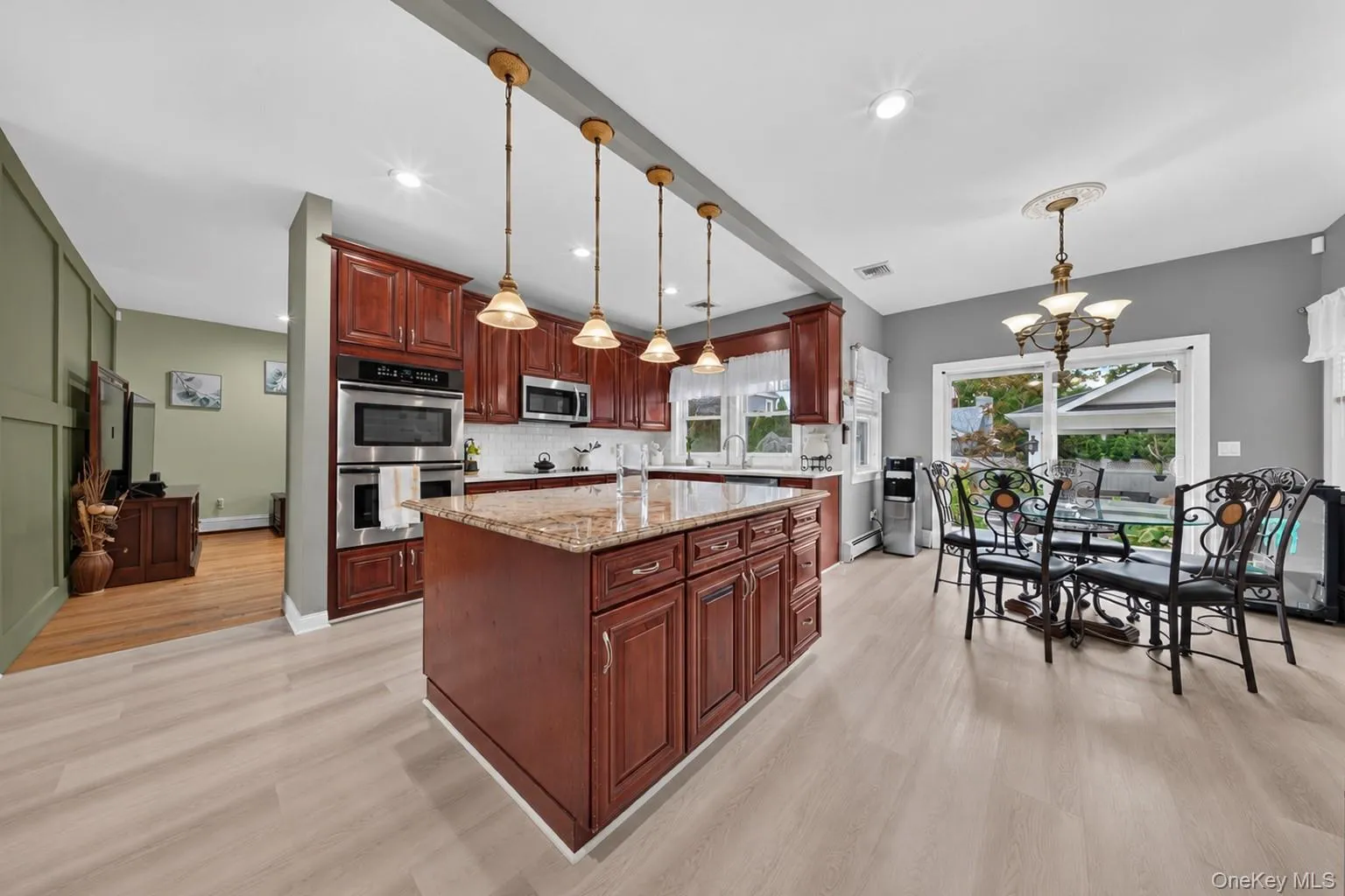 Kitchen featuring wood cabinetry, stainless steel appliances, a center island with a stone countertop, and light wood-finish flooring Kitchen featuring wood cabinetry, stainless steel appliances, a center island with a stone countertop, and light wood-finish flooring