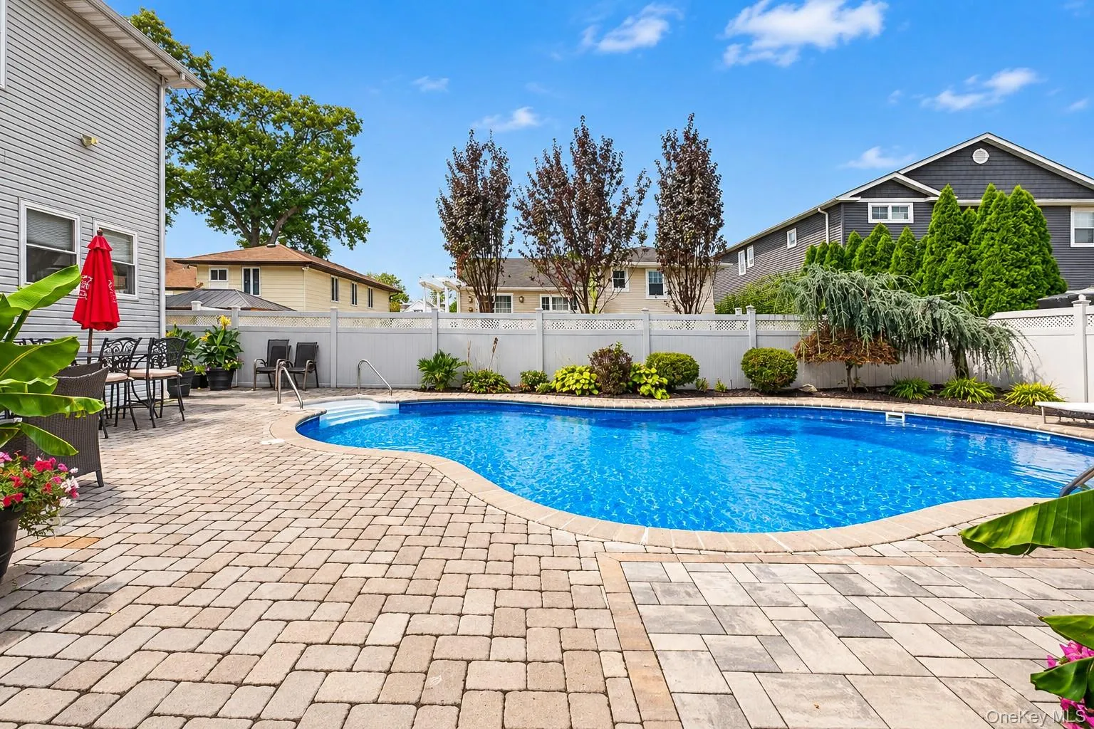 Backyard featuring a freeform swimming pool, extensive paver patio, and white privacy fencing Backyard featuring a freeform swimming pool, extensive paver patio, and white privacy fencing