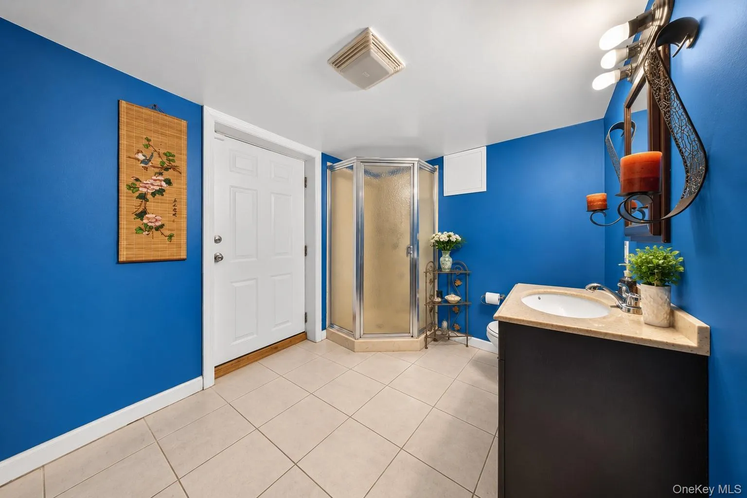 Tiled flooring, corner shower enclosure, dark wood-finish vanity, light-toned countertop, and a single-panel door Tiled flooring, corner shower enclosure, dark wood-finish vanity, light-toned countertop, and a single-panel door