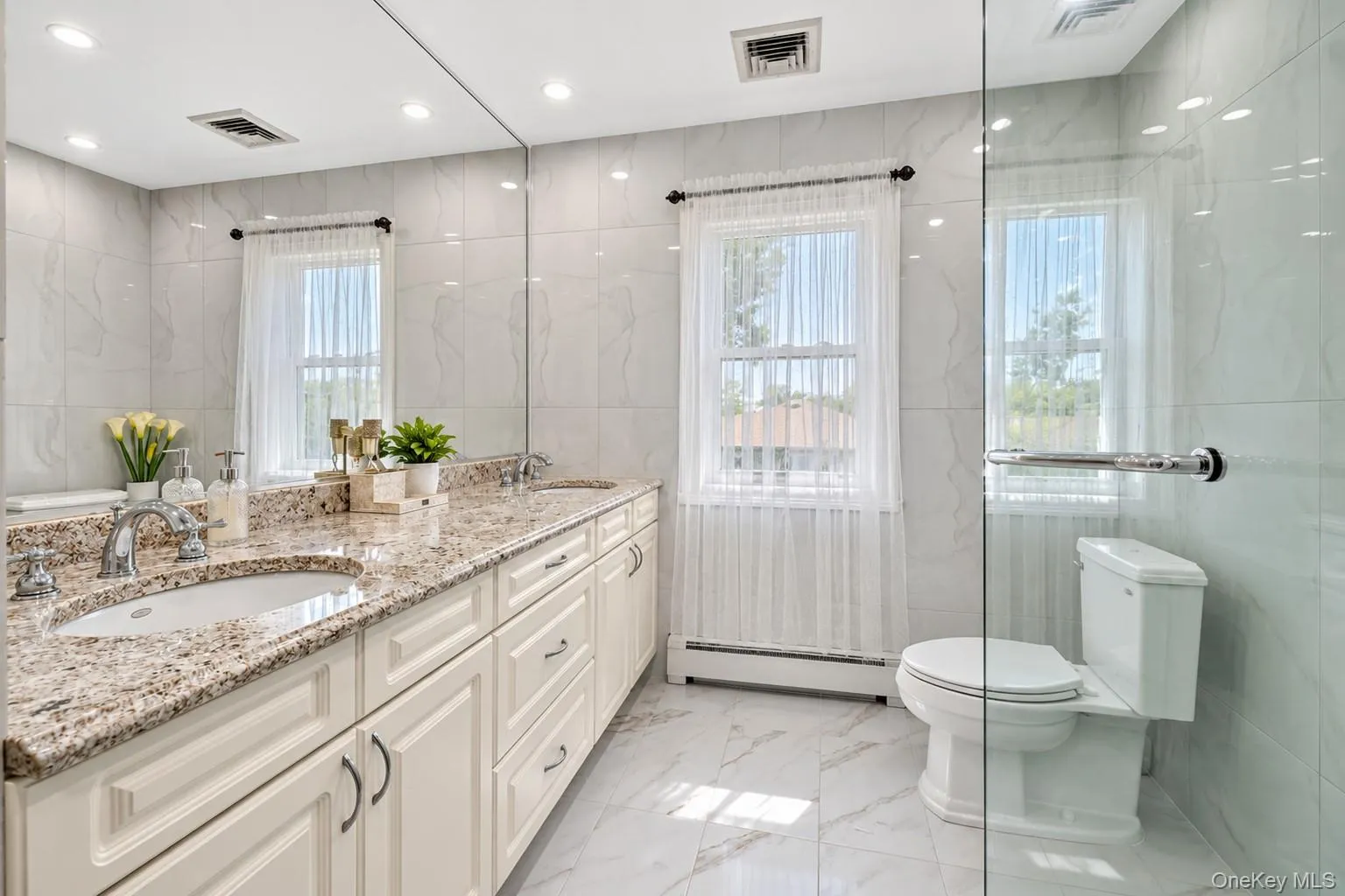 Dual vanity with granite countertop, tiled walls, large mirror, recessed lighting, and glass-enclosed shower Dual vanity with granite countertop, tiled walls, large mirror, recessed lighting, and glass-enclosed shower