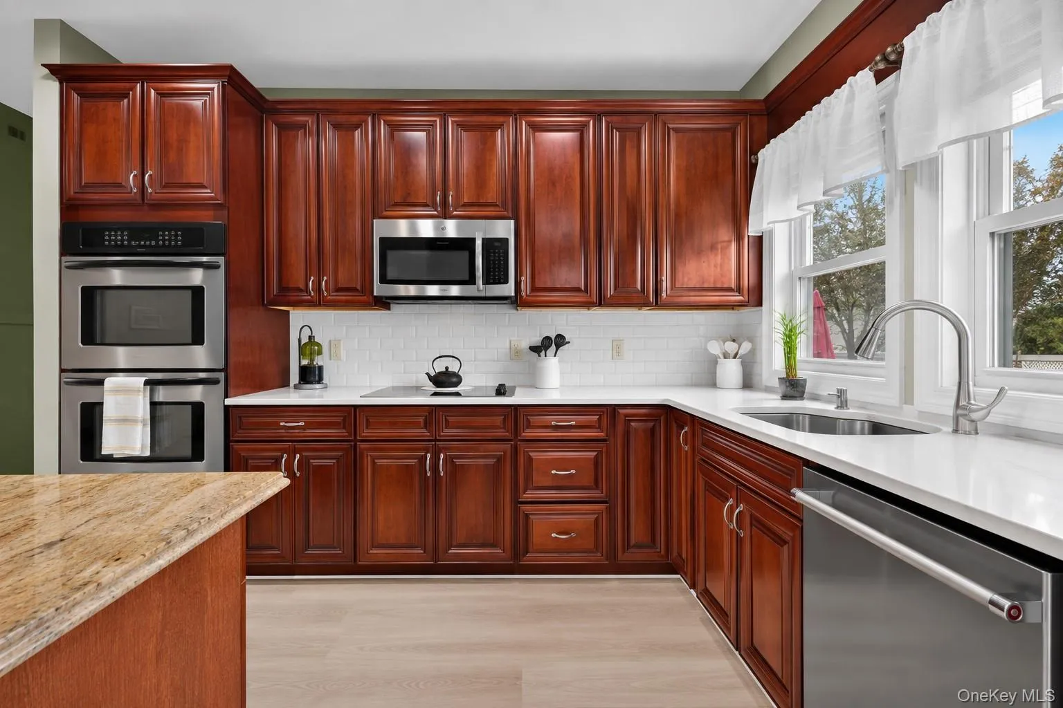 Kitchen featuring rich wood cabinetry, stainless steel appliances including double wall ovens and a built-in microwave, white subway tile backsplash, and light-toned countertops Kitchen featuring rich wood cabinetry, stainless steel appliances including double wall ovens and a built-in microwave, white subway tile backsplash, and light-toned countertops