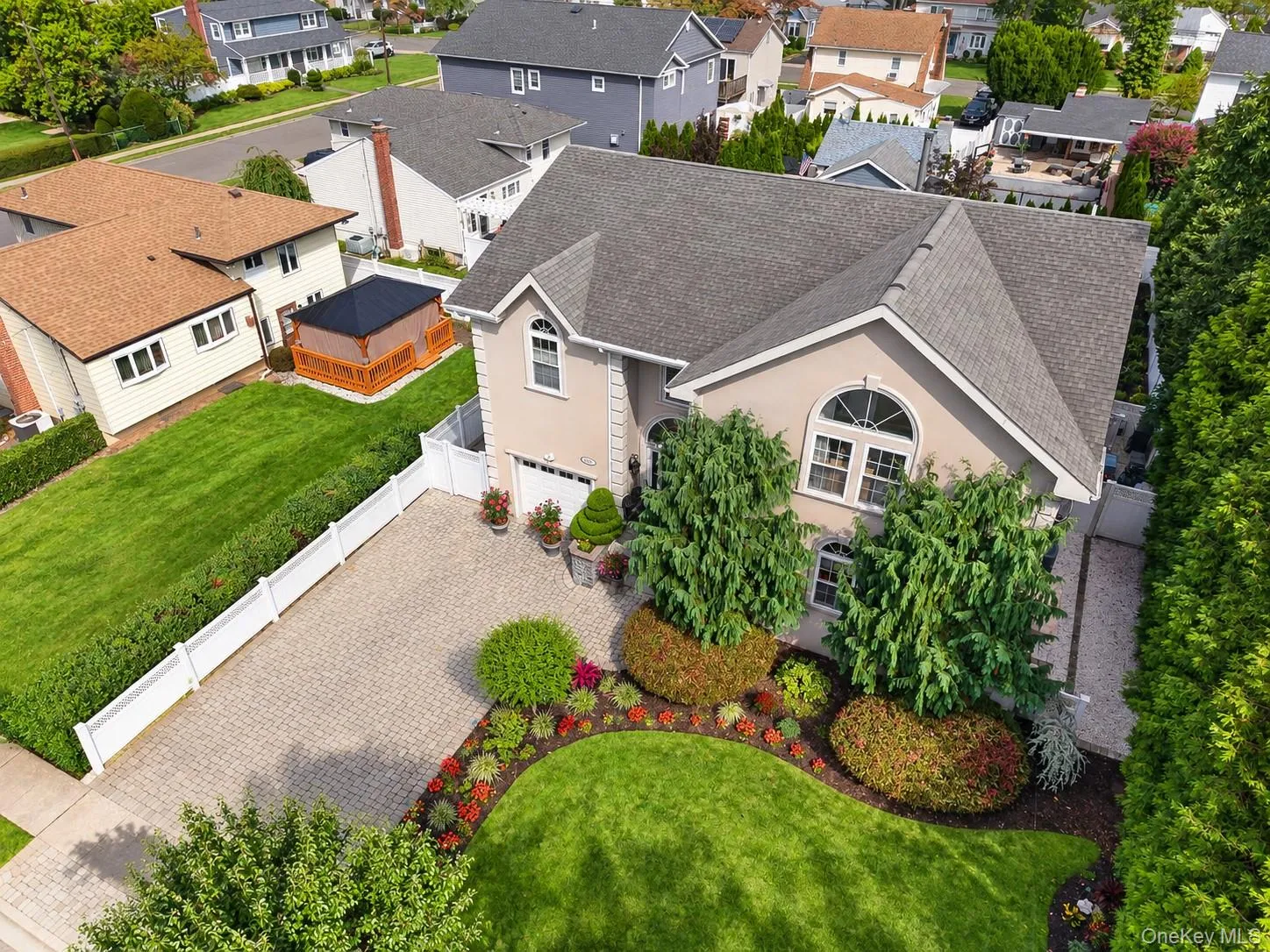 Stucco exterior with arched window detailing, paved driveway, mature landscaping, and privacy fencing Stucco exterior with arched window detailing, paved driveway, mature landscaping, and privacy fencing
