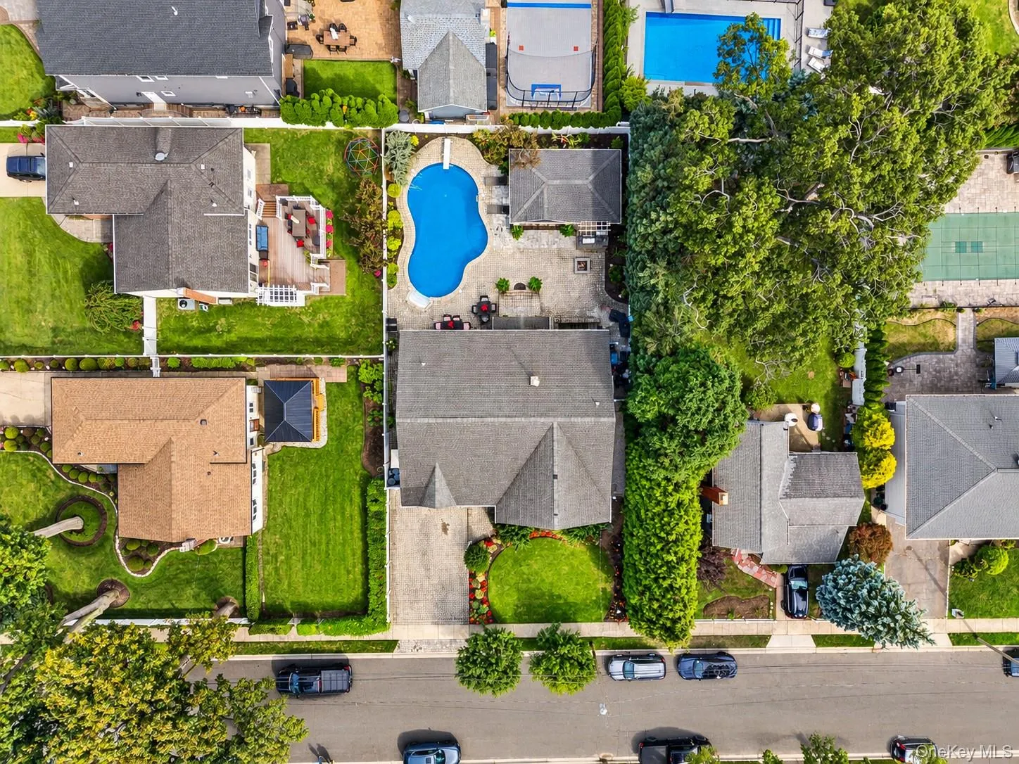 Residential property featuring a swimming pool, paved patio, expansive lawn, mature trees, and a paved driveway Residential property featuring a swimming pool, paved patio, expansive lawn, mature trees, and a paved driveway