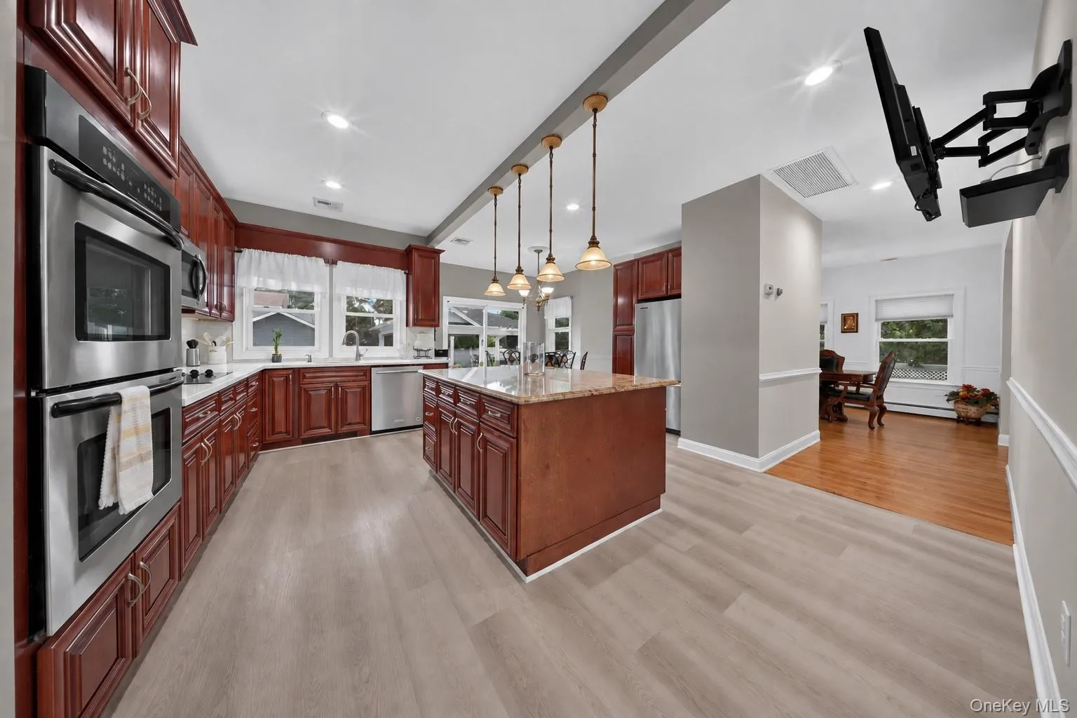 Kitchen featuring wood cabinetry, stainless steel appliances, a center island with a stone-finish countertop, pendant lighting, and wood-finish flooring Kitchen featuring wood cabinetry, stainless steel appliances, a center island with a stone-finish countertop, pendant lighting, and wood-finish flooring