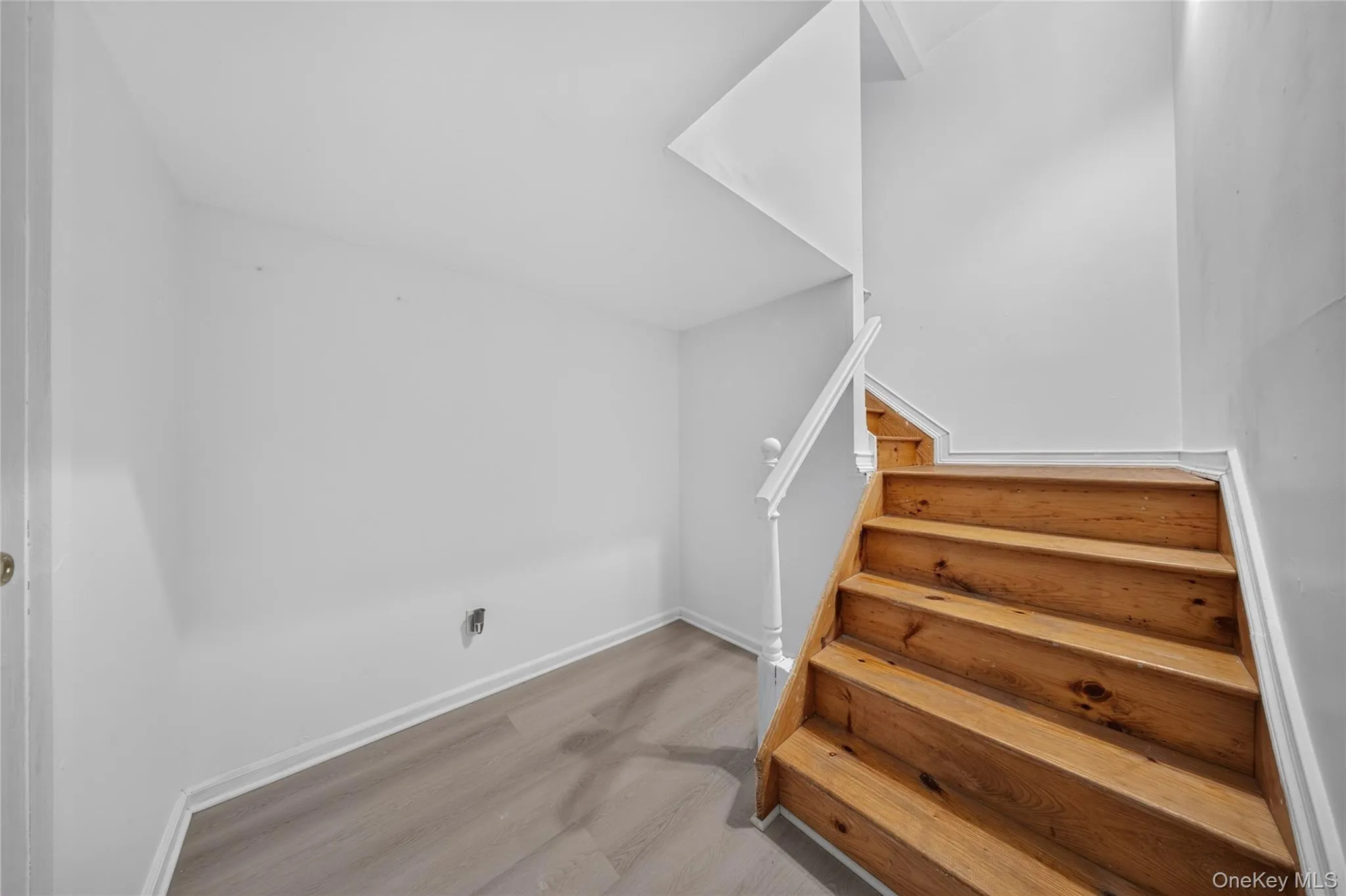 Wood-finish flooring, natural wood staircase, white painted walls, white railing with balusters, and white trim Wood-finish flooring, natural wood staircase, white painted walls, white railing with balusters, and white trim