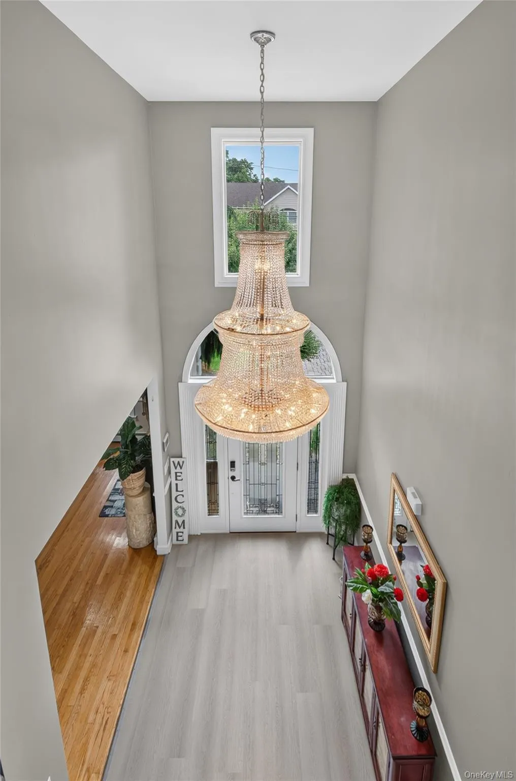 Two-story foyer featuring a large chandelier, wood-finish flooring, and a white entry door with glass panels Two-story foyer featuring a large chandelier, wood-finish flooring, and a white entry door with glass panels