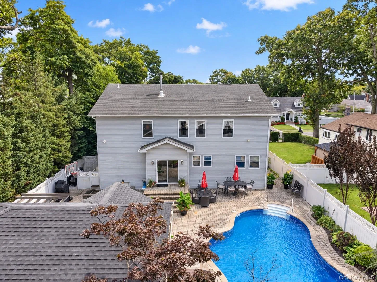 Rear exterior featuring a freeform pool, paver patio, white privacy fencing, and mature trees Rear exterior featuring a freeform pool, paver patio, white privacy fencing, and mature trees
