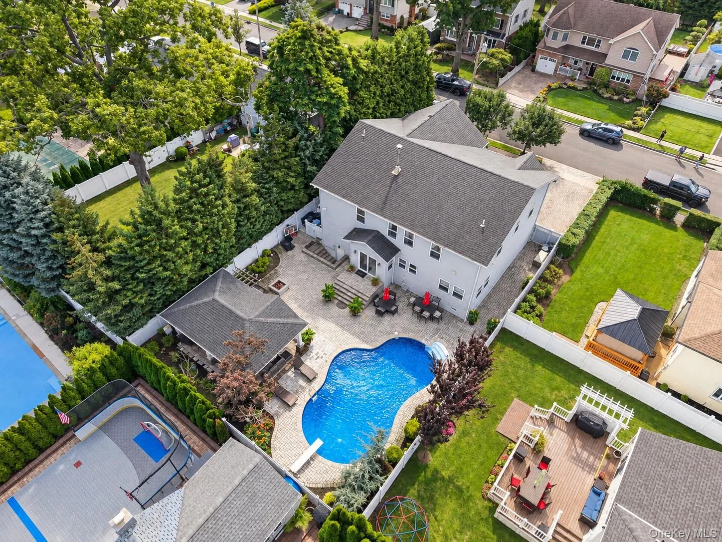 Two-story exterior with a gray siding finish, a large inground swimming pool, a stone patio, a covered gazebo, and a spacious rear deck Two-story exterior with a gray siding finish, a large inground swimming pool, a stone patio, a covered gazebo, and a spacious rear deck