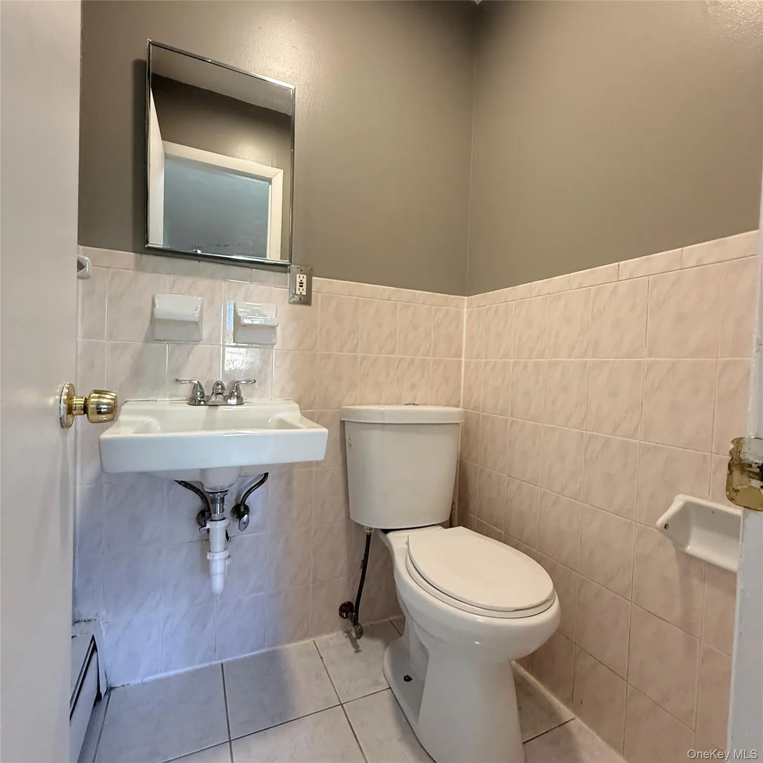 Wall-mounted sink with chrome faucet, ceramic tile walls, and square ceramic floor tiles Wall-mounted sink with chrome faucet, ceramic tile walls, and square ceramic floor tiles