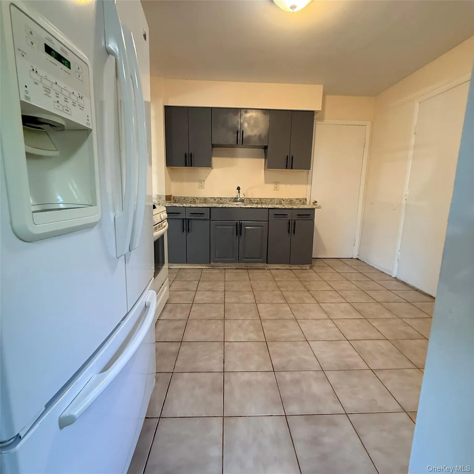 White side-by-side refrigerator, gray cabinetry with black hardware, light-toned countertop, and light-toned floor tiling White side-by-side refrigerator, gray cabinetry with black hardware, light-toned countertop, and light-toned floor tiling