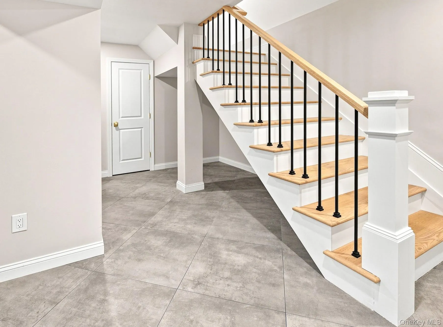 Lower level staircase featuring wood treads, black iron balusters, a natural wood handrail, and white risers. Lower level staircase featuring wood treads, black iron balusters, a natural wood handrail, and white risers.