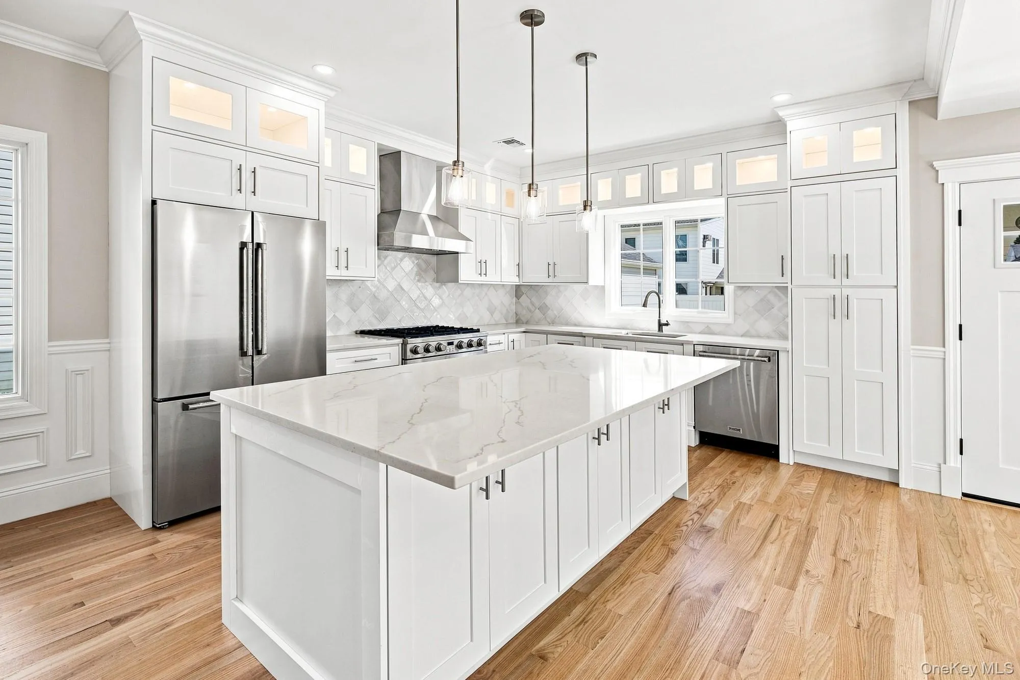 Gourmet Kitchen with a large center island featuring a white quartz countertop, stainless steel appliances, white shaker cabinetry, and wood-finish flooring Gourmet Kitchen with a large center island featuring a white quartz countertop, stainless steel appliances, white shaker cabinetry, and wood-finish flooring