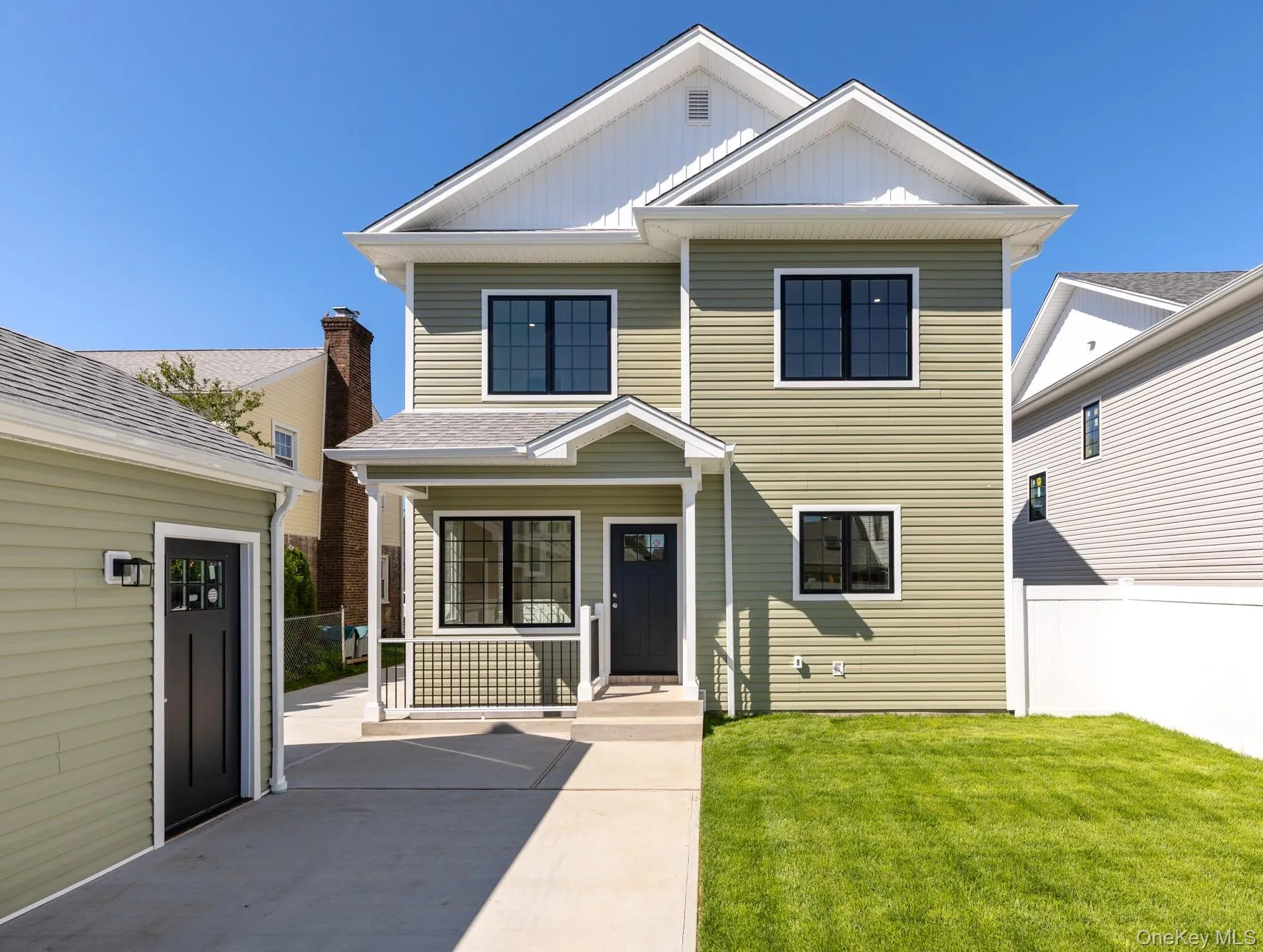 Sunny view of residence featuring light green siding, black-framed windows, and a covered entrance and steps to lower level with a railing. Sunny view of residence featuring light green siding, black-framed windows, and a covered entrance and steps to lower level with a railing.