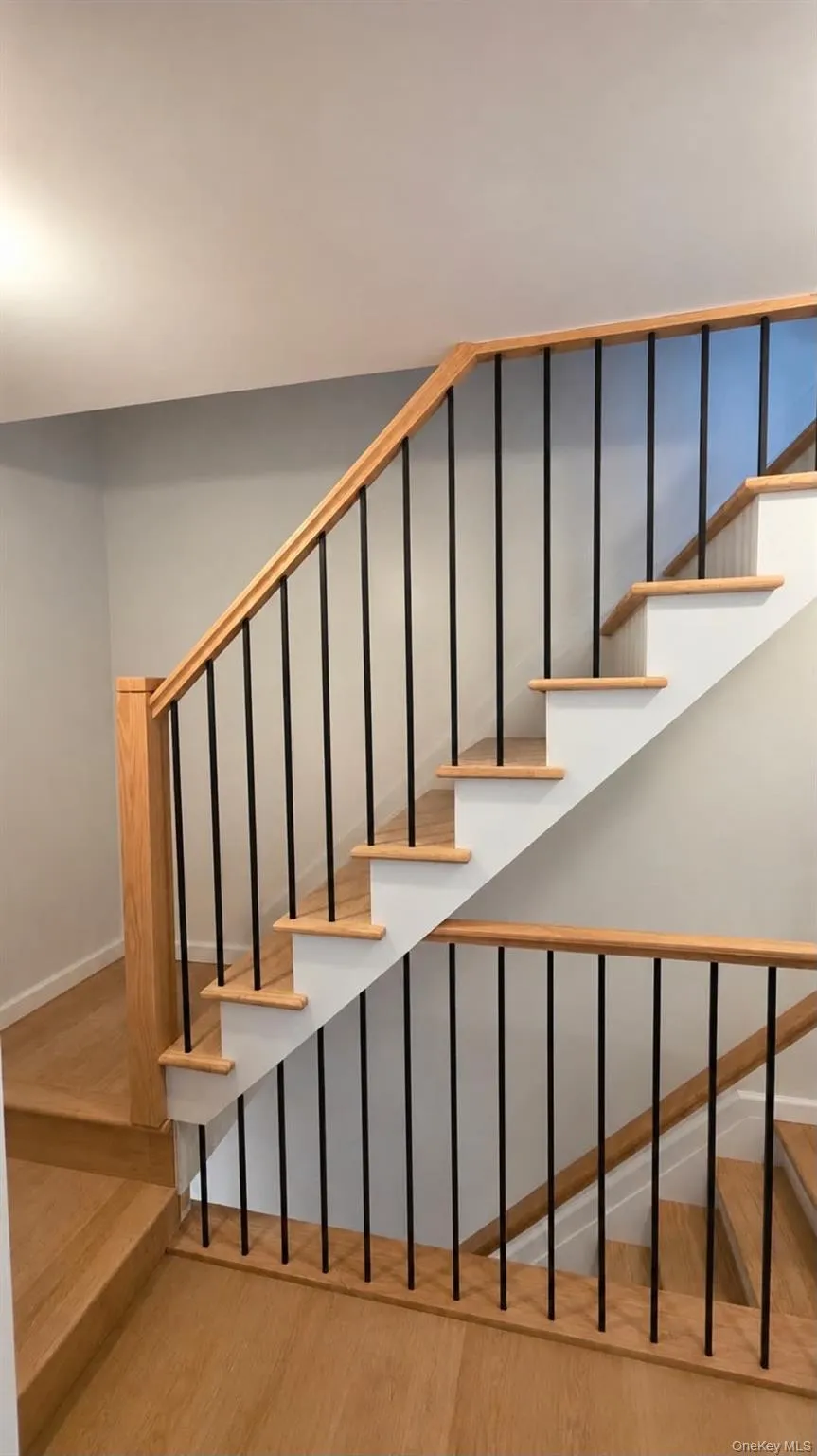 Hardwood flooring extending to stair treads, contrasting white risers, and black metal balusters with wood handrails Hardwood flooring extending to stair treads, contrasting white risers, and black metal balusters with wood handrails