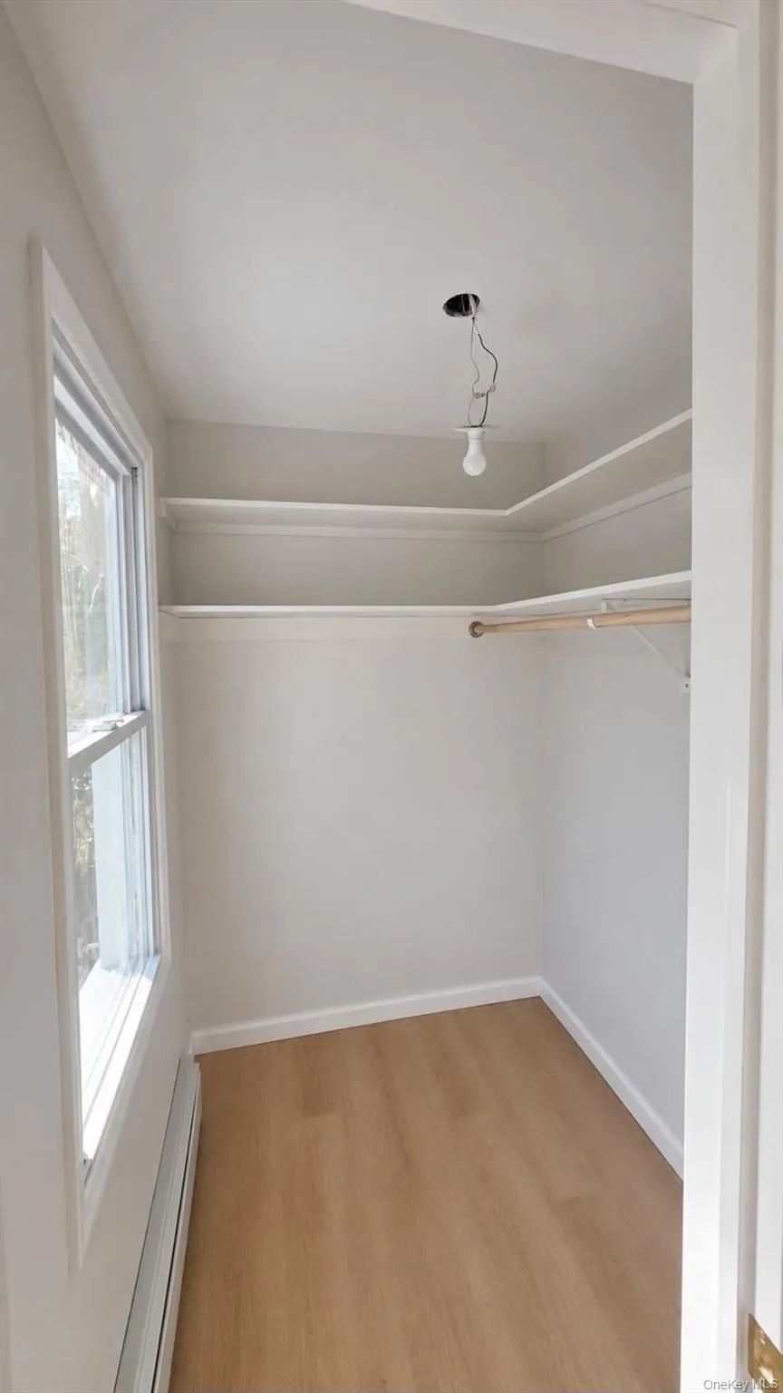 Built-in shelving, hanging rod, wood-finish flooring, and a single window Built-in shelving, hanging rod, wood-finish flooring, and a single window