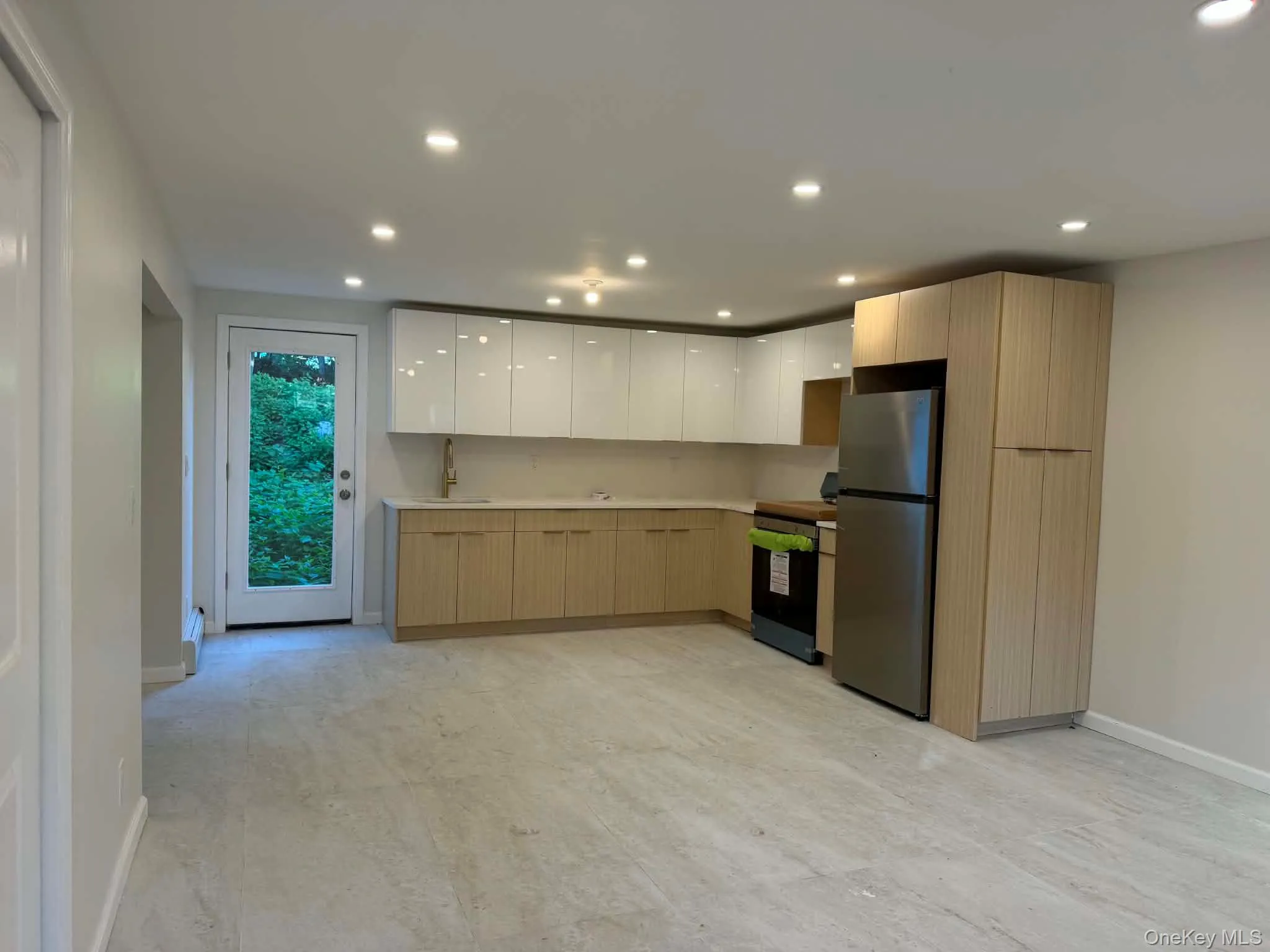 Recessed lighting illuminating the open-concept kitchen featuring light wood-finish lower cabinetry, white upper cabinetry, light-toned countertops, and stainless steel appliances Recessed lighting illuminating the open-concept kitchen featuring light wood-finish lower cabinetry, white upper cabinetry, light-toned countertops, and stainless steel appliances