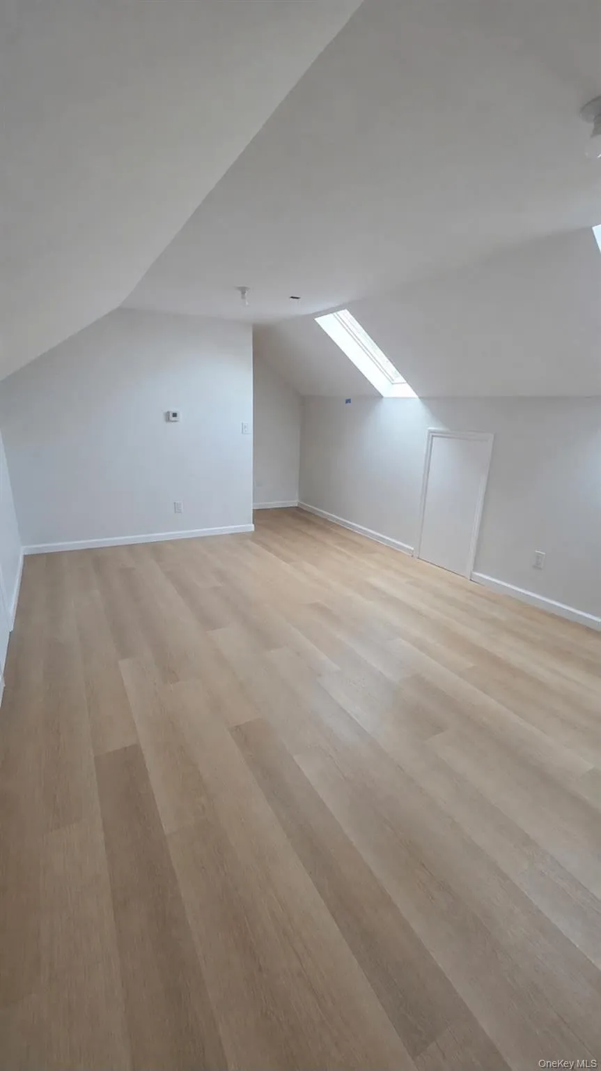 Finished attic with slanted ceiling with skylight, wood-finish flooring, and white painted walls Finished attic with slanted ceiling with skylight, wood-finish flooring, and white painted walls