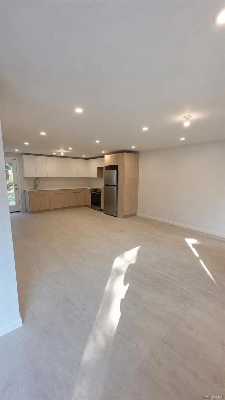Recessed lighting, wood-finish cabinetry, stainless steel appliances, light-toned flooring, and a rear exterior door Recessed lighting, wood-finish cabinetry, stainless steel appliances, light-toned flooring, and a rear exterior door
