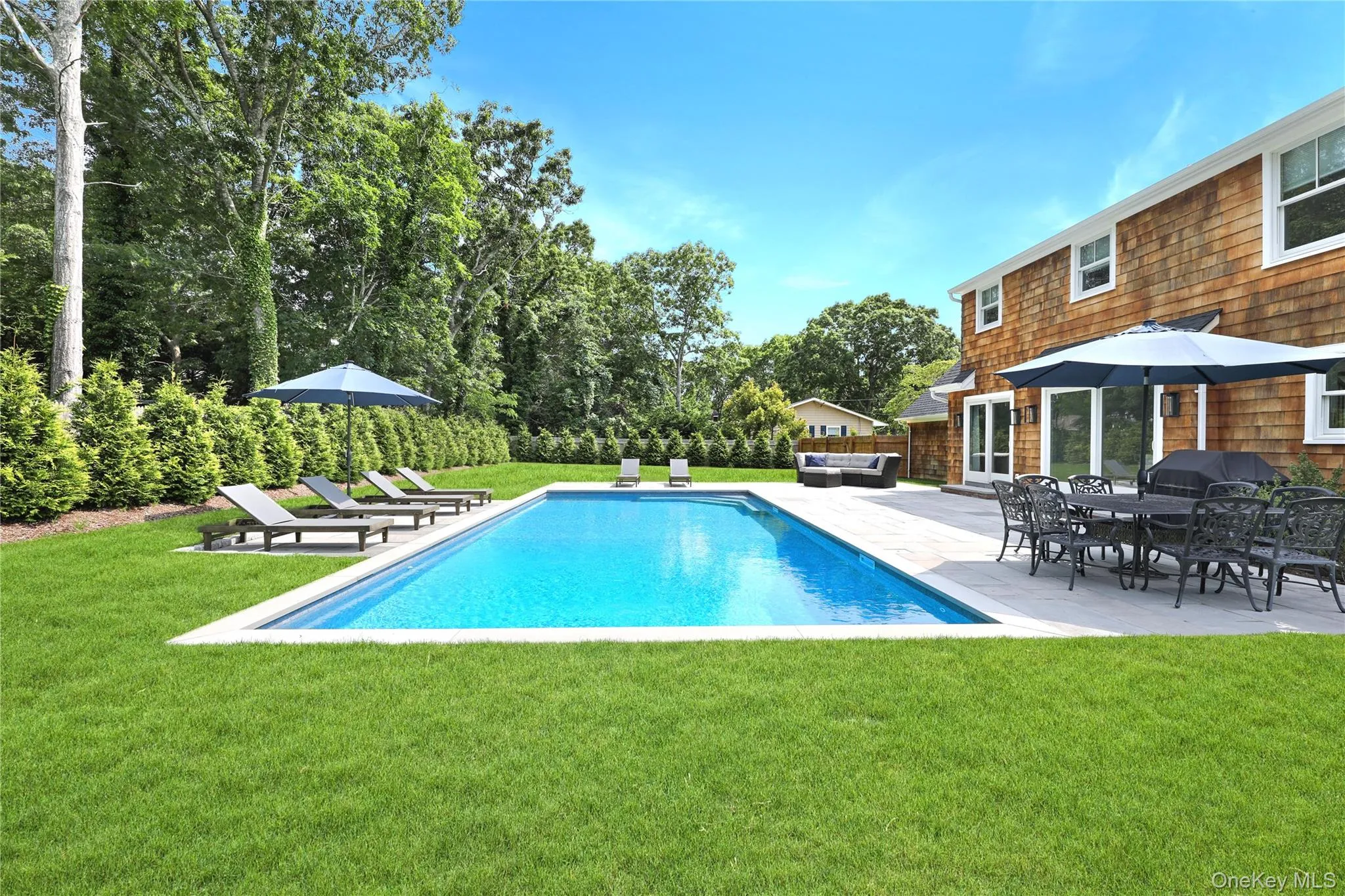 Outdoor pool with a patio, a lawn, outdoor lounge area, and view of wooded area Outdoor pool with a patio, a lawn, outdoor lounge area, and view of wooded area